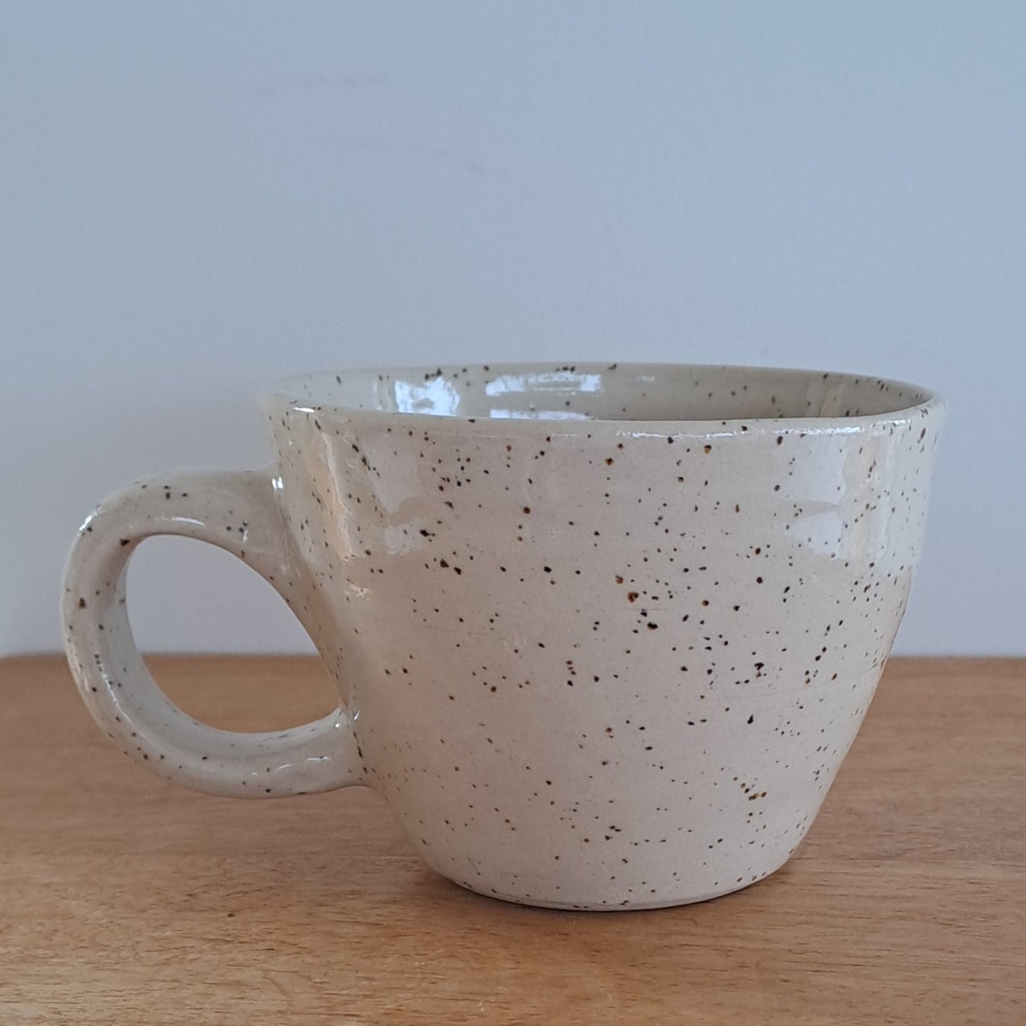 Speckled ceramic cup on a wooden surface with a light gray background