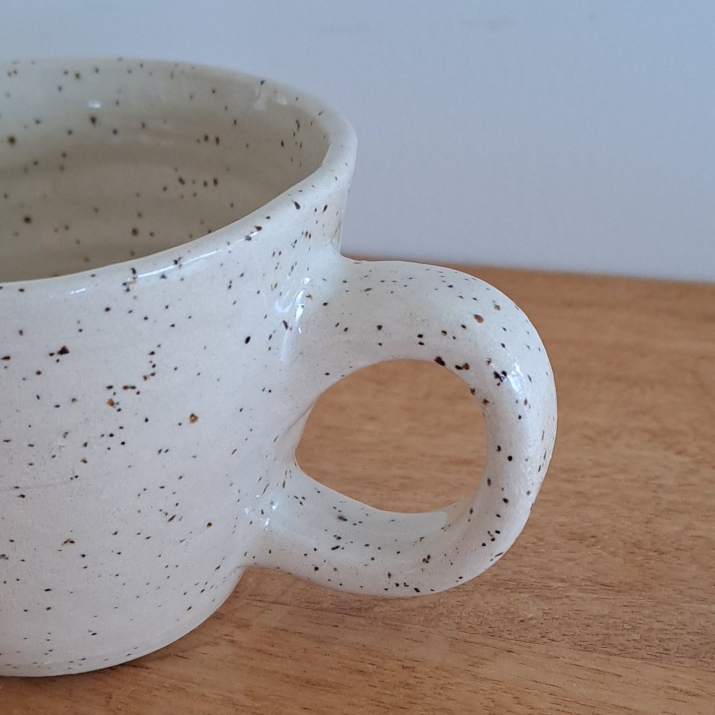 Speckled ceramic mug on a wooden surface with a light gray background