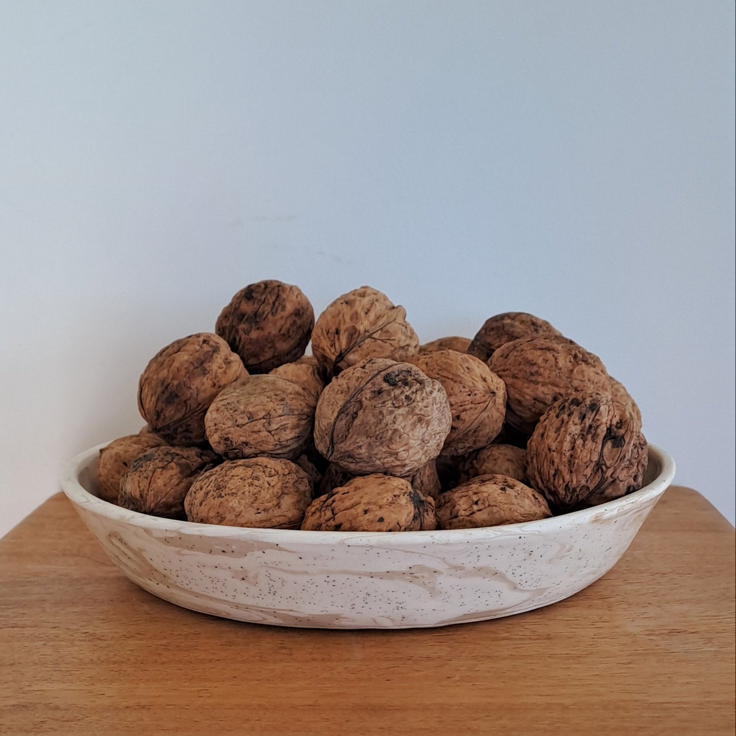 Bowl filled with walnuts on a wooden shelf against a white wall