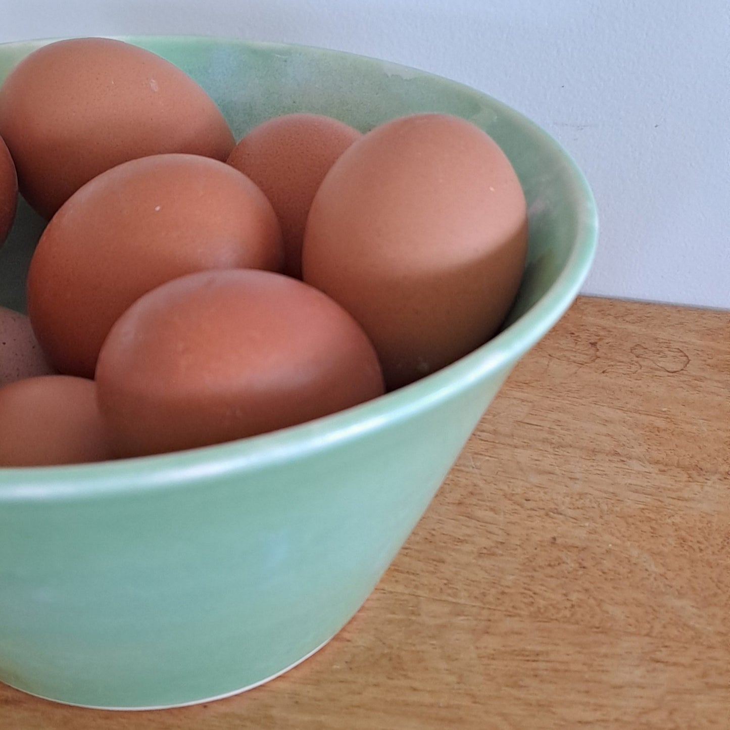 Green ceramic bowl with brown eggs on a wooden surface