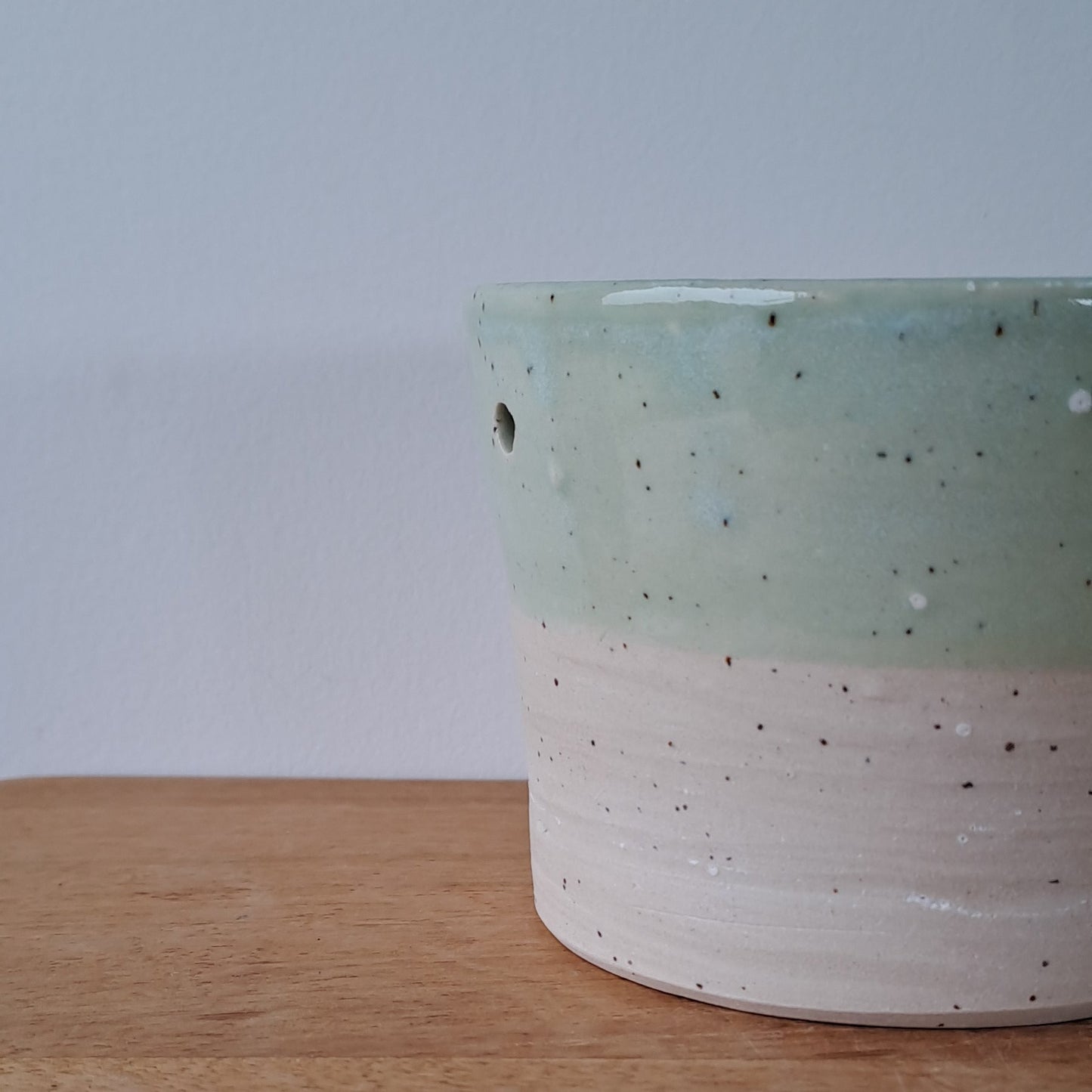 Ceramic speckled planter with blue green glaze on wooden table with light background