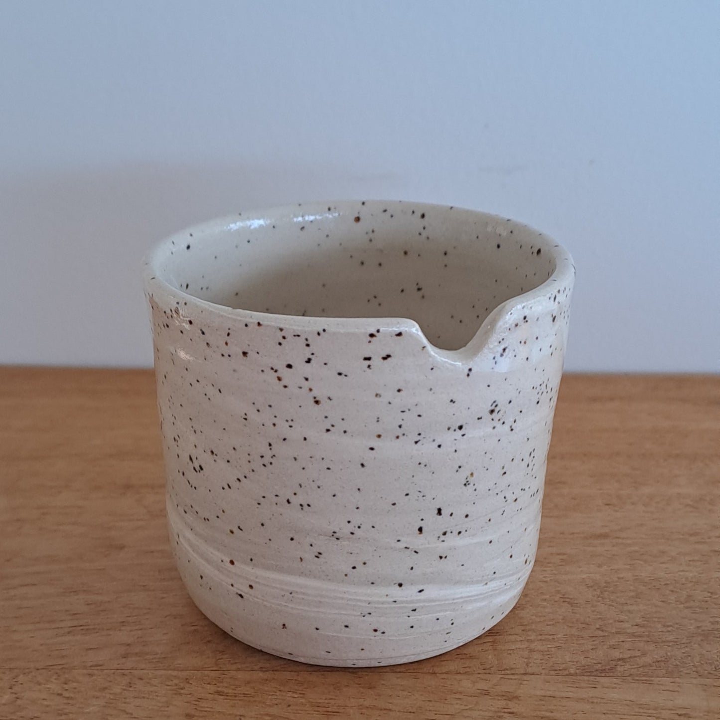 Speckled ceramic cup on a wooden surface with a light blue background