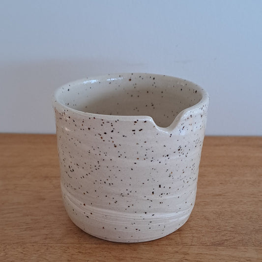 Speckled ceramic cup on a wooden surface with a light blue background