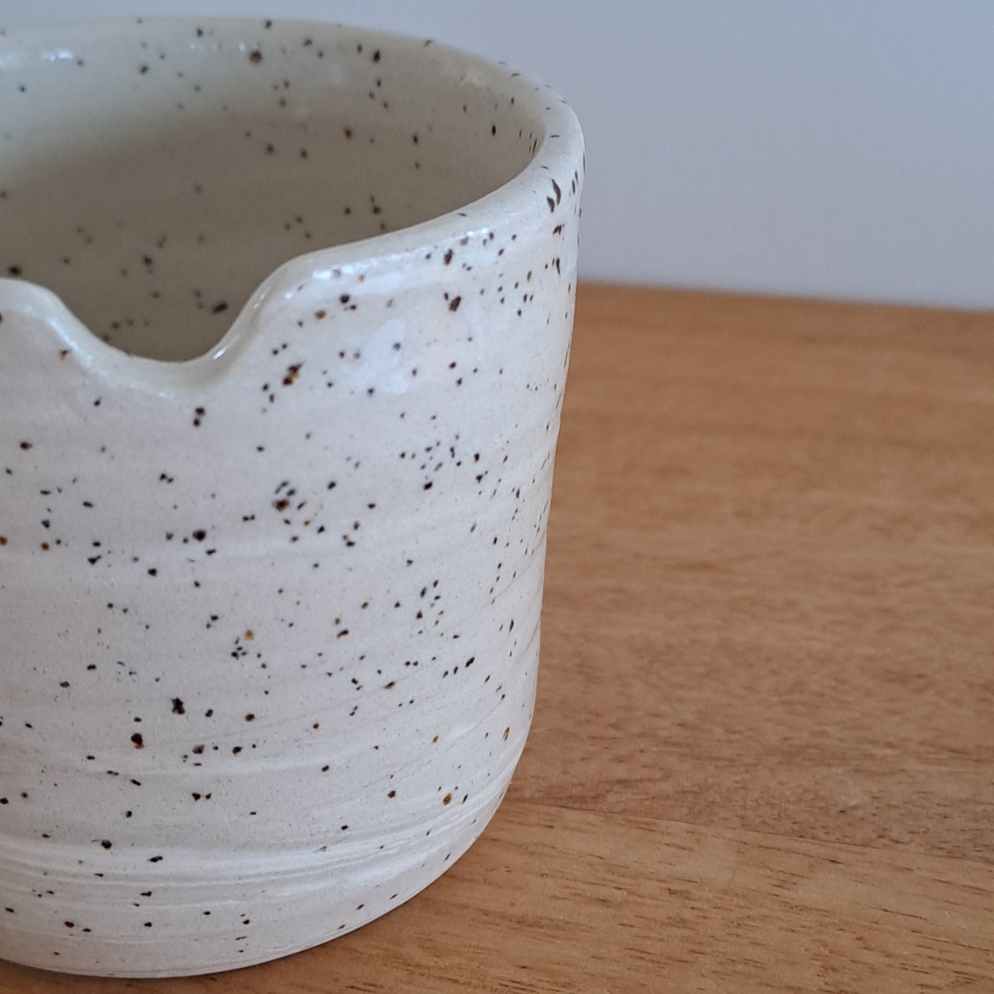 Speckled ceramic cup on a wooden surface with a white background