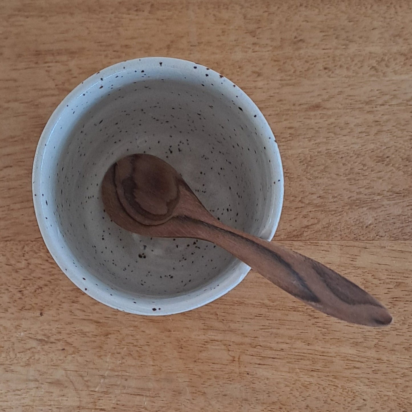 Speckled ceramic cup with a wooden spoon on a wooden surface