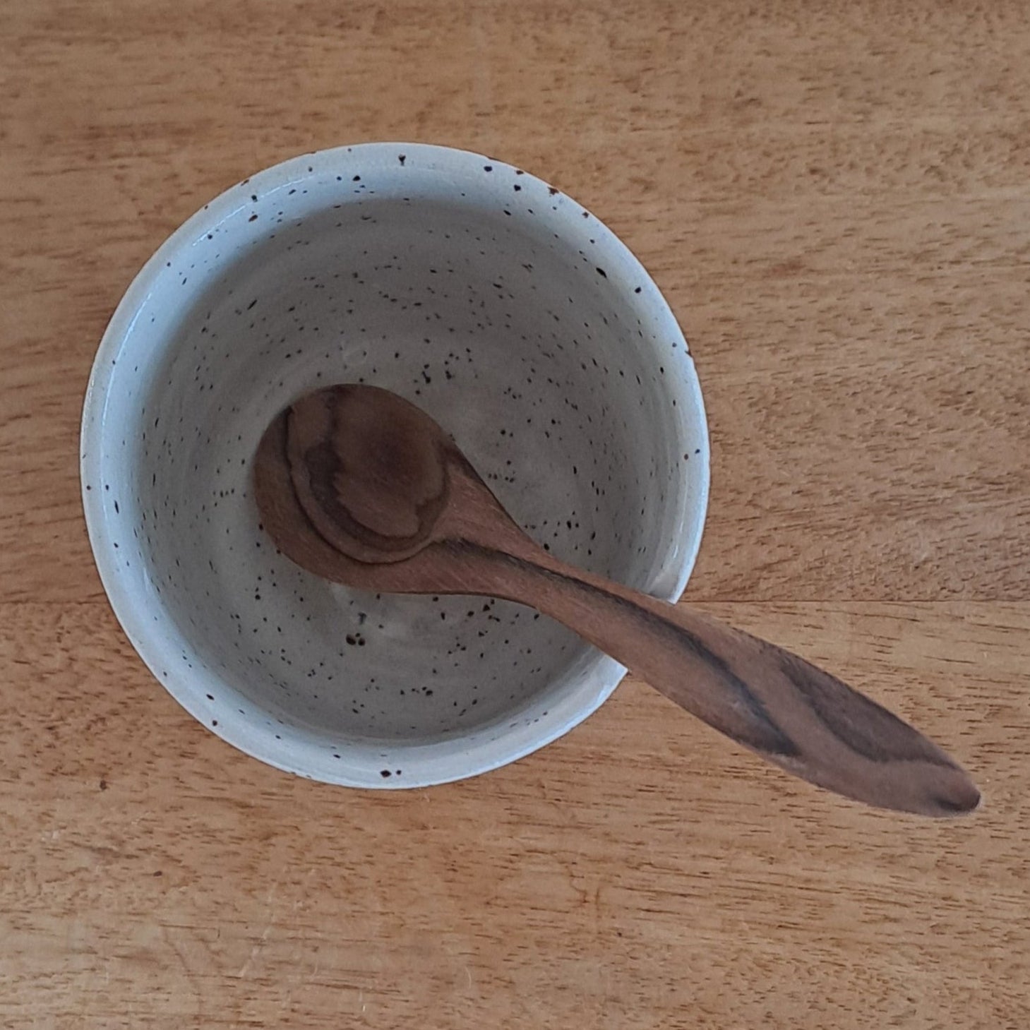 Speckled ceramic cup with a wooden spoon on a wooden surface