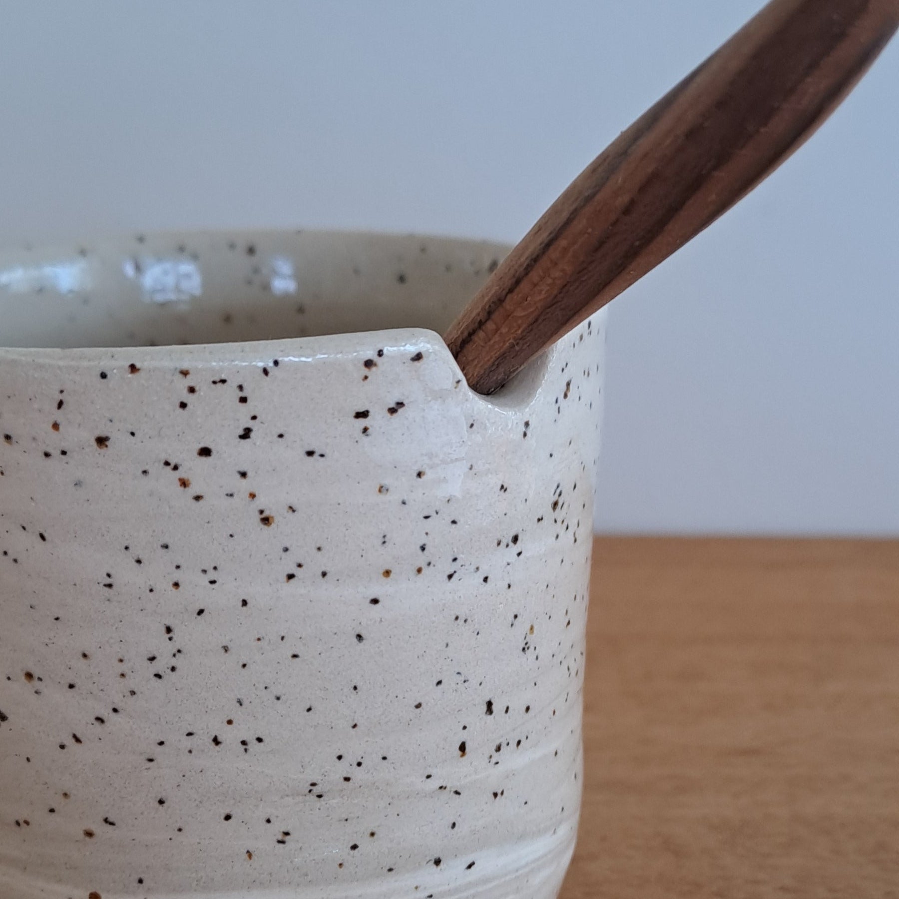 Speckled ceramic mug with wooden handle on a light wood surface