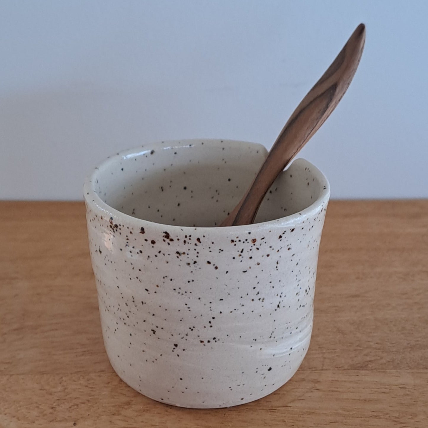 Small ceramic cup with a wooden stick on a light wood surface