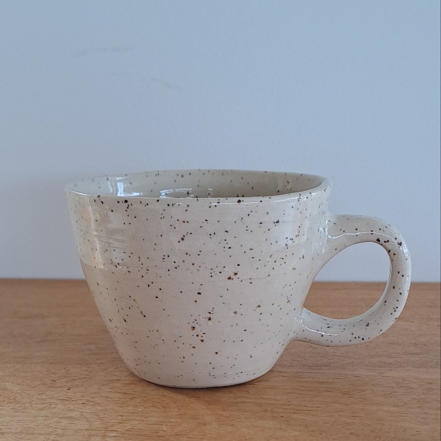 Speckled ceramic cup hanging on a wooden surface with a light background
