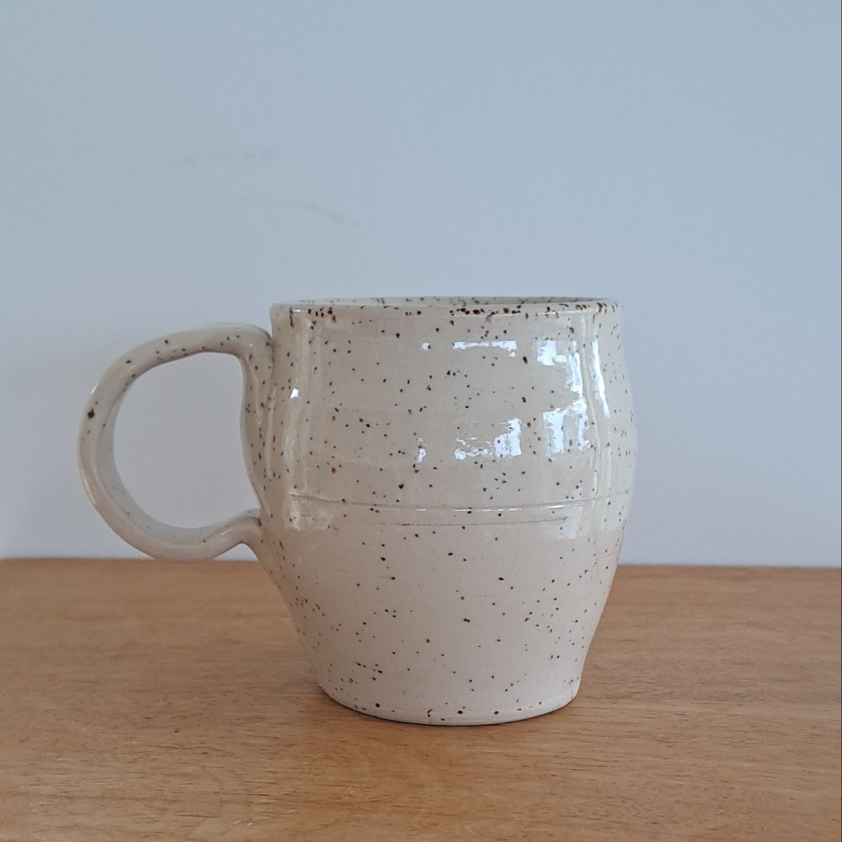 Speckled ceramic mug on a wooden surface with a white background