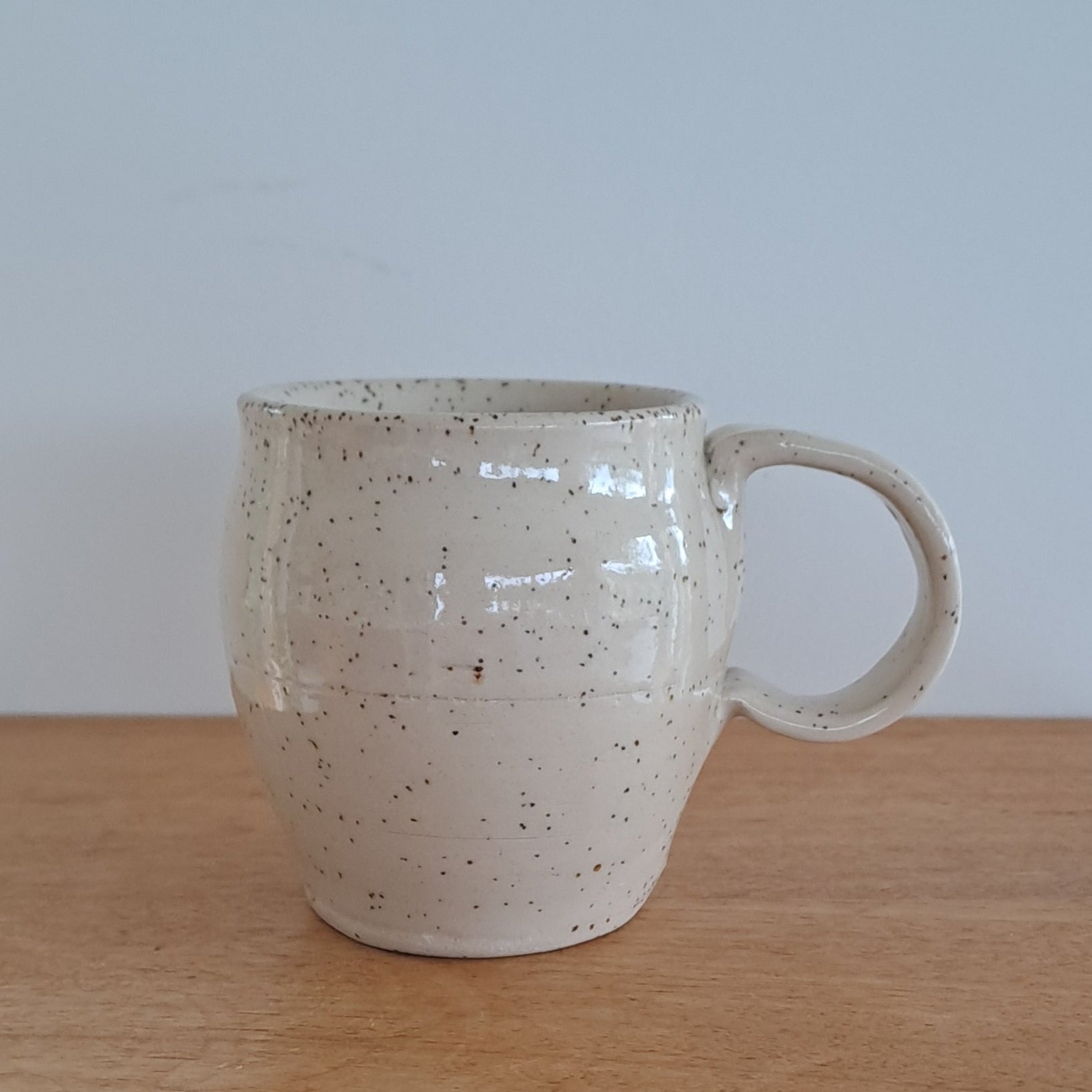 Speckled ceramic mug attached to a wooden surface with a light wall in the background