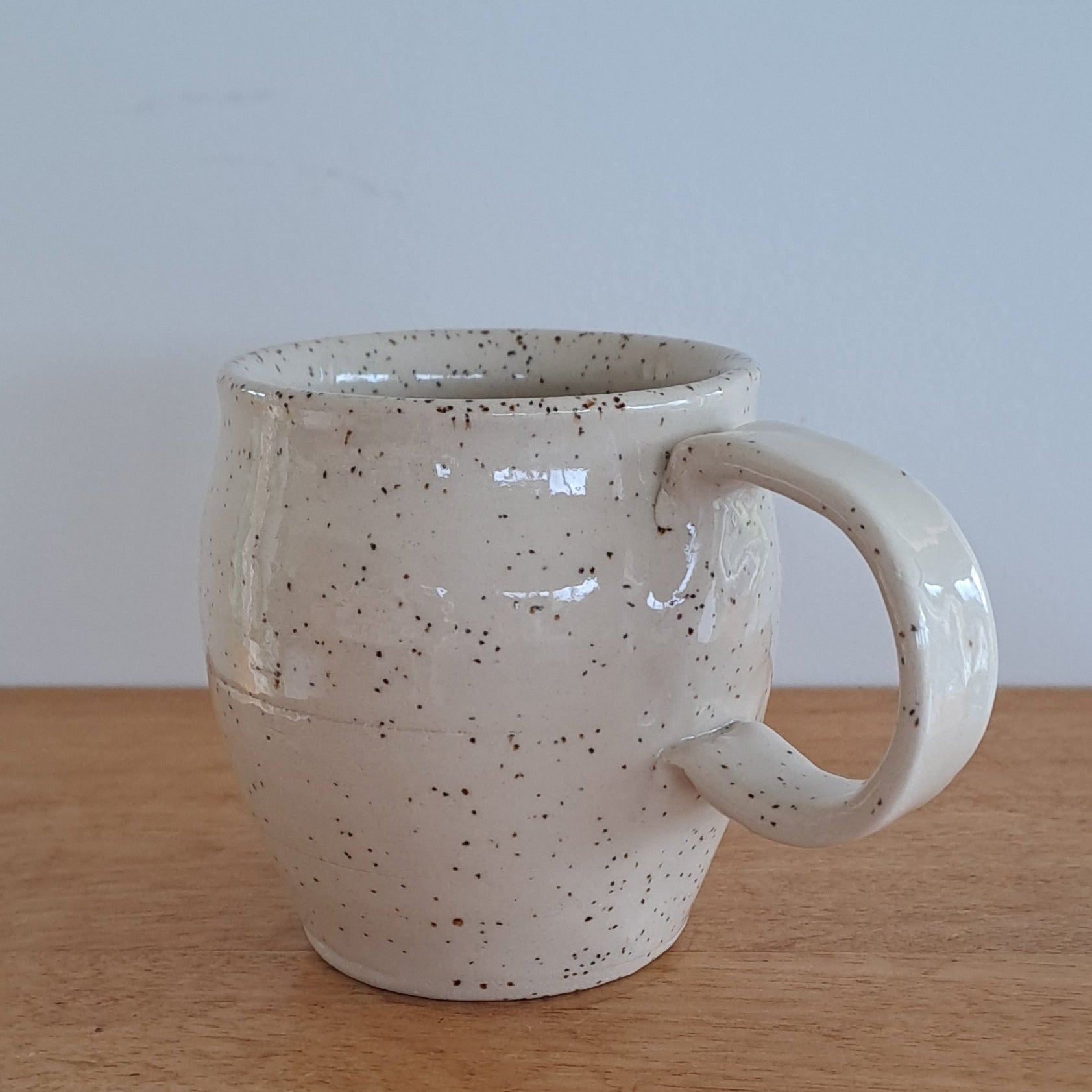 White ceramic mug with speckled texture on a wooden surface