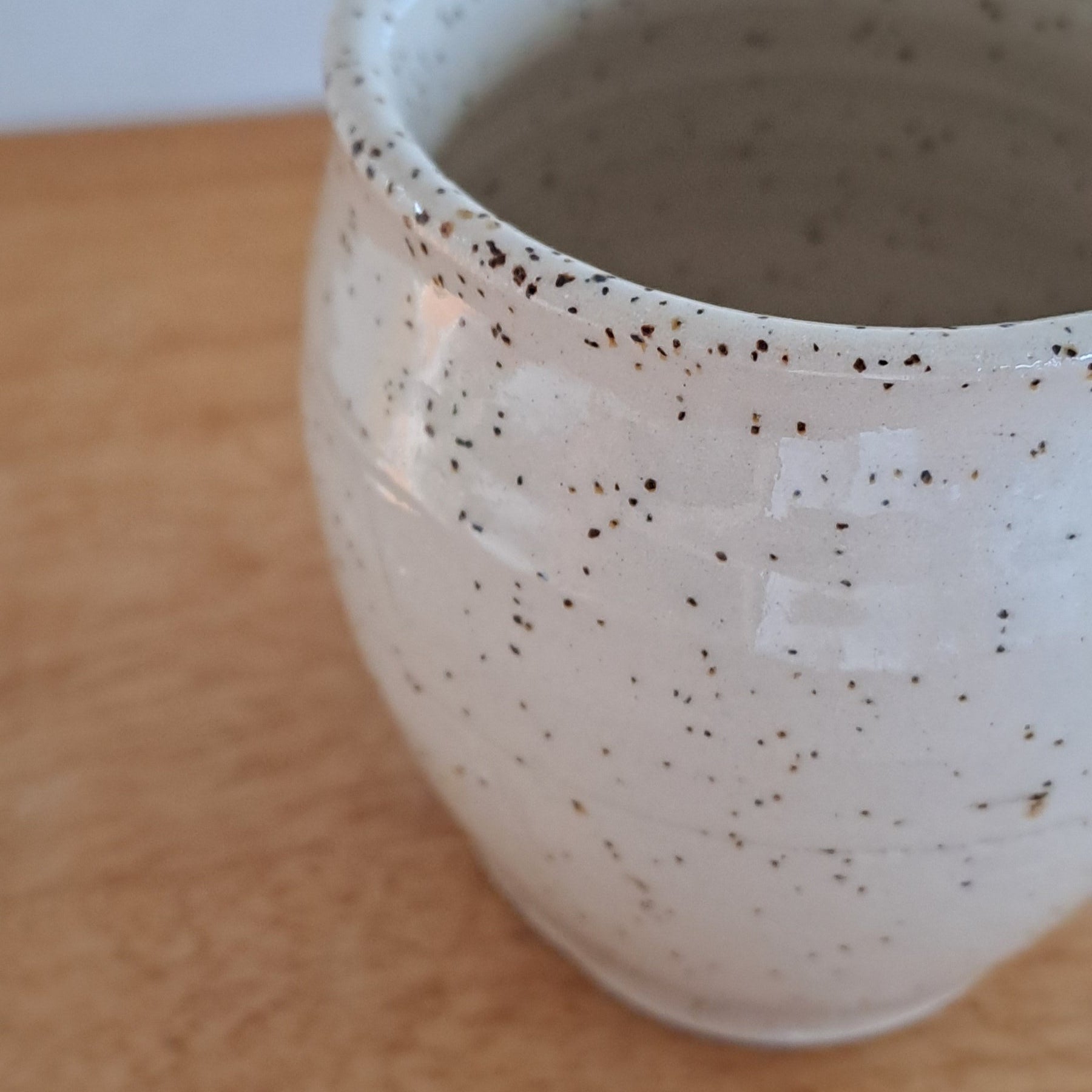 Speckled ceramic cup on a wooden surface with a white background