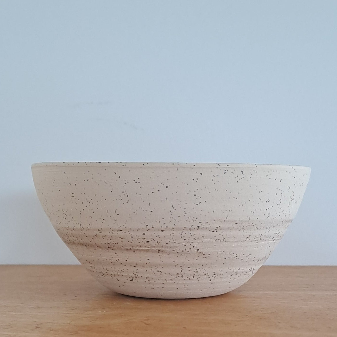 Speckled ceramic bowl on a wooden surface with a light blue background