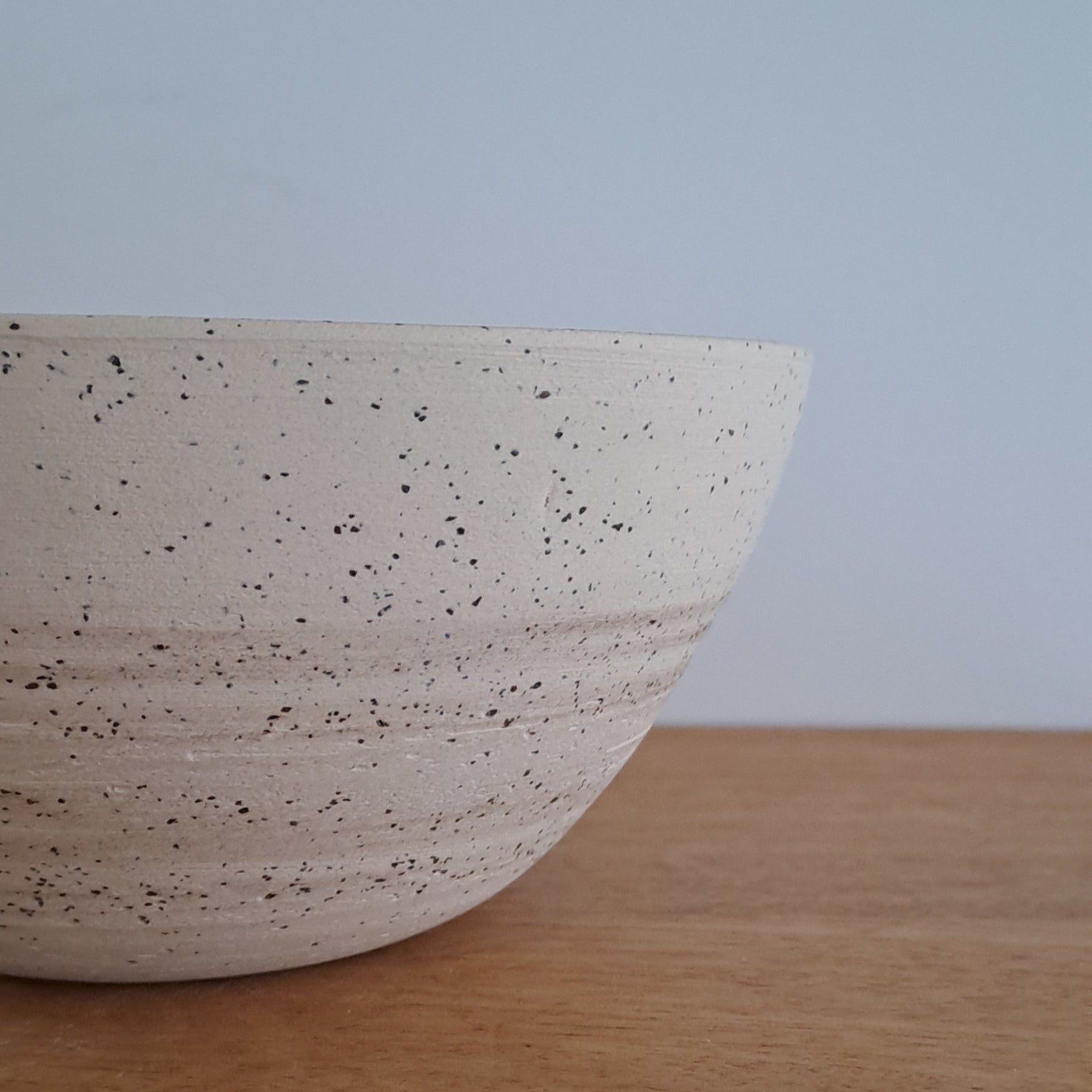 Close-up of a ceramic bowl with a wooden surface and light blue background