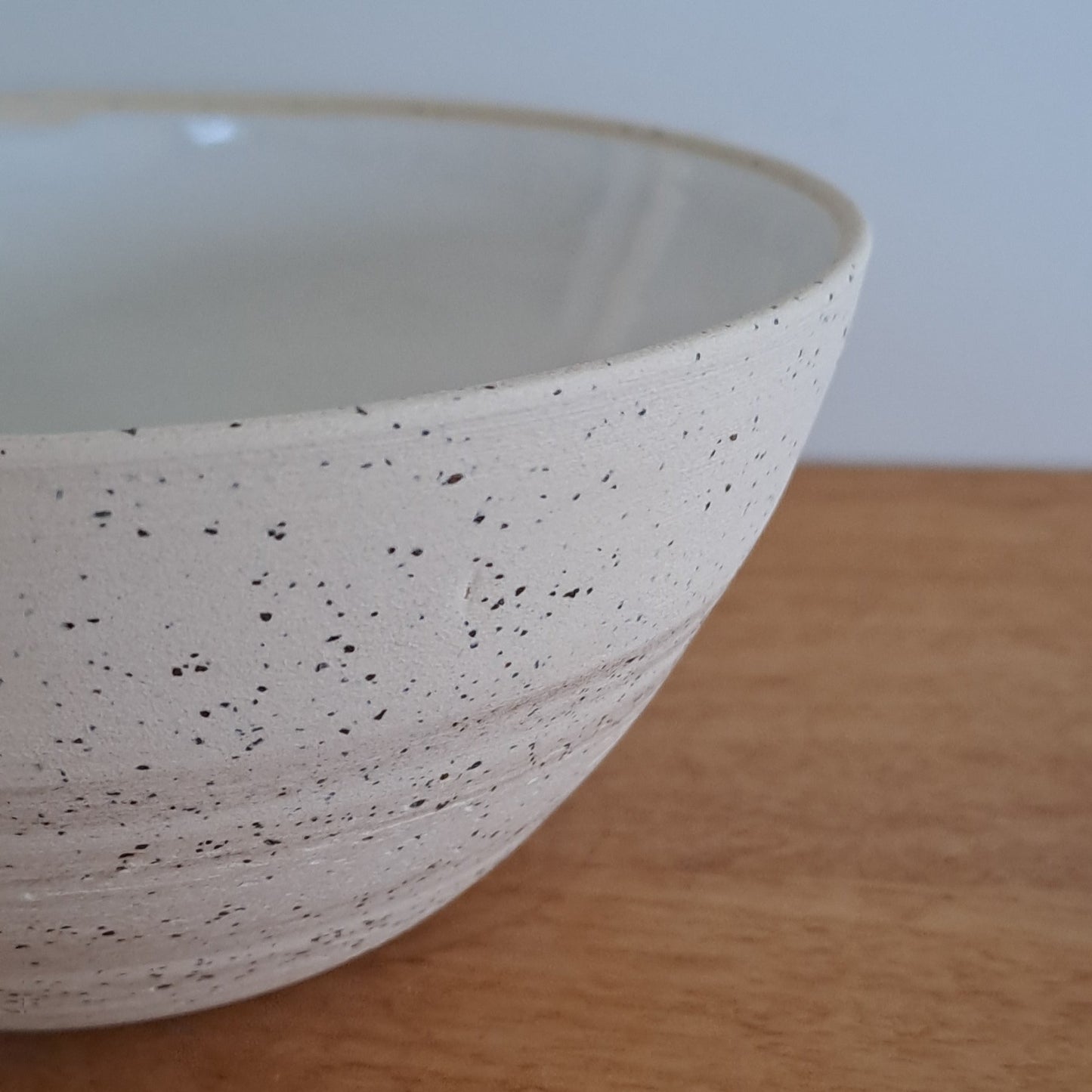 Speckled ceramic bowl leaning against a wooden surface with a neutral background