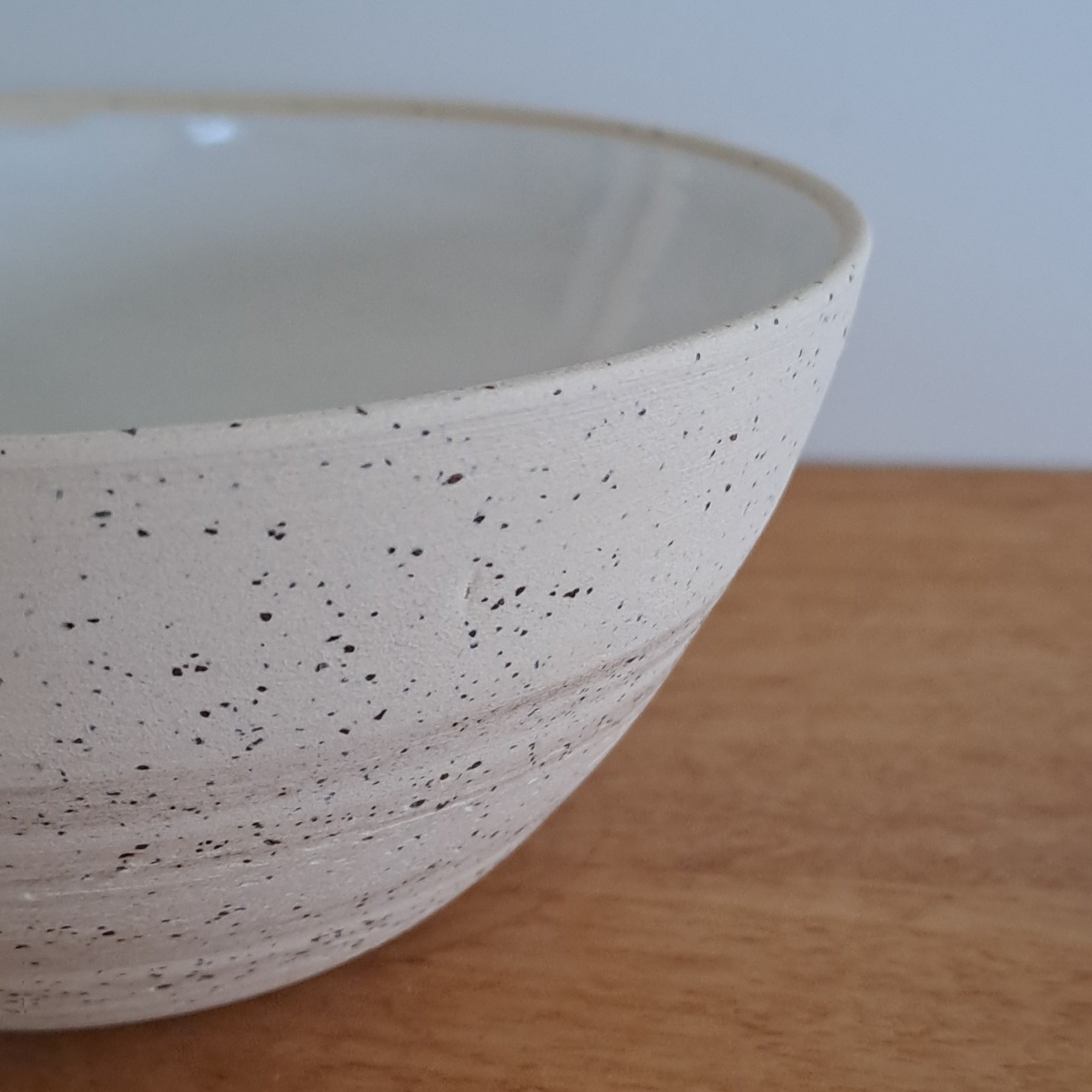 Speckled ceramic bowl leaning against a wooden surface with a neutral background