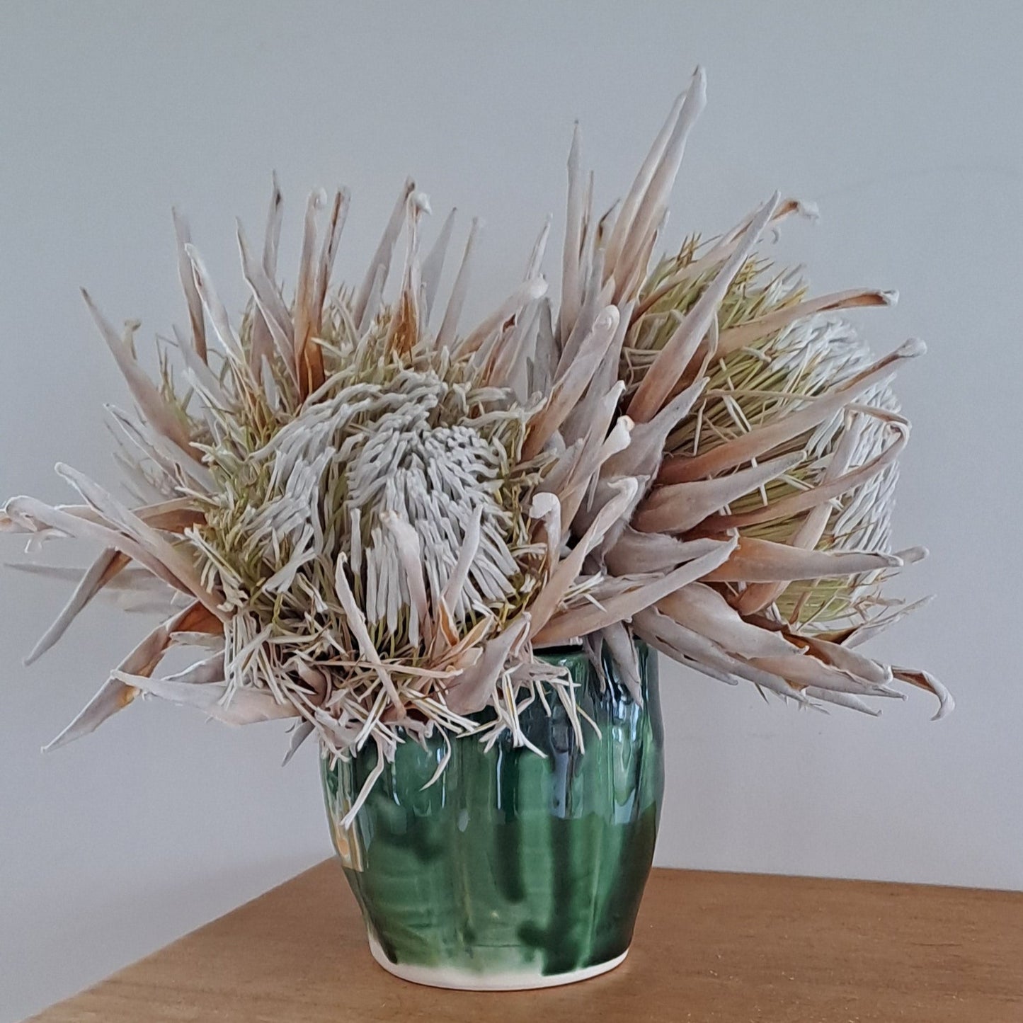 Decorative flower arrangement in a green vase on a wooden chair with a plain background