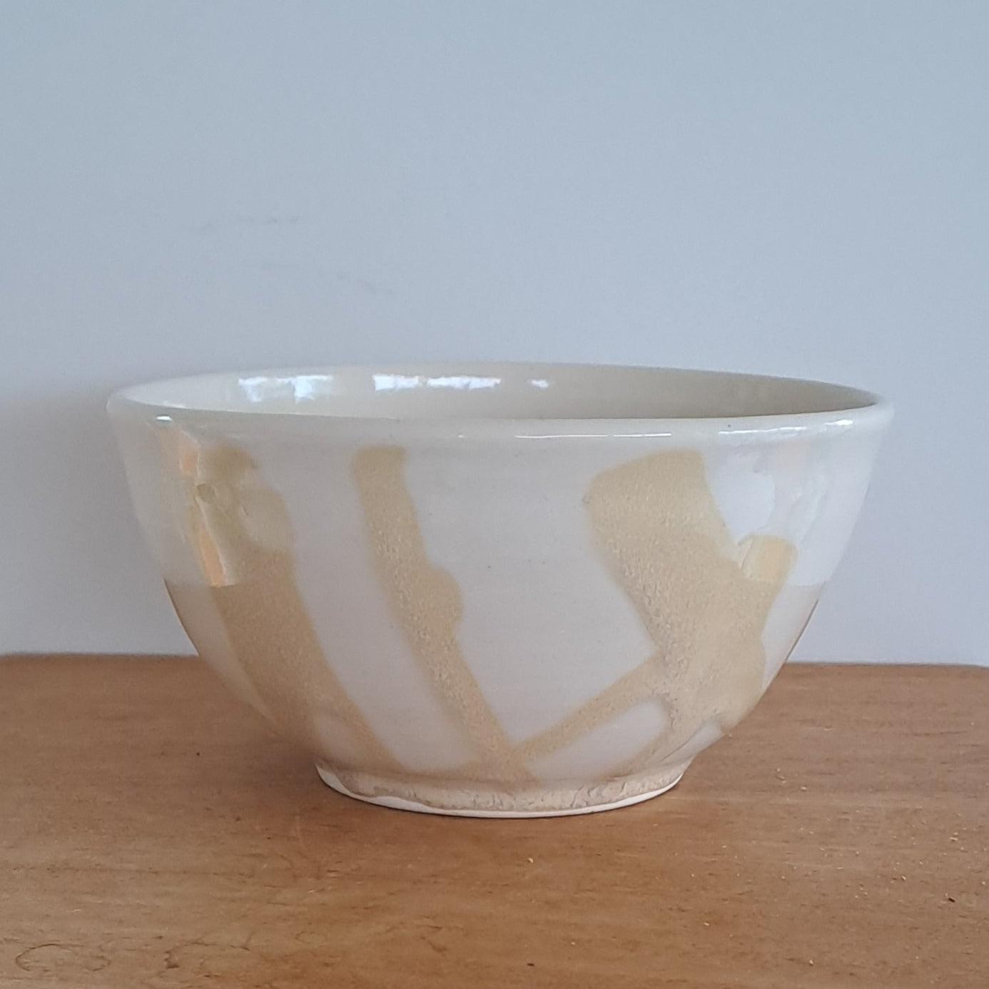 Wooden stool with a ceramic bowl on top against a white wall.