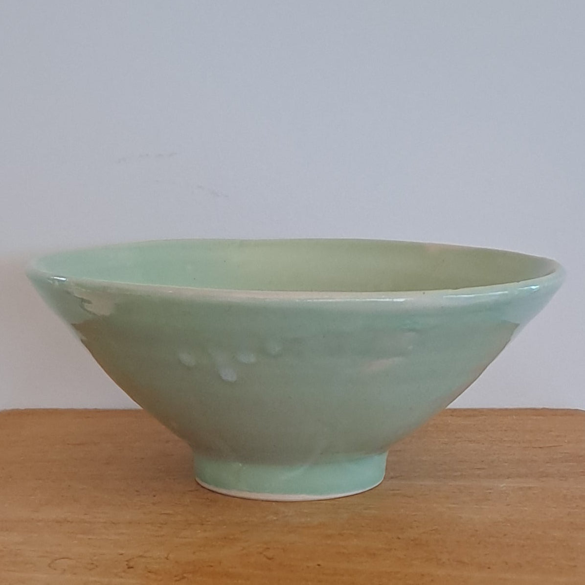 green ceramic bowl on a wooden stool against a white background