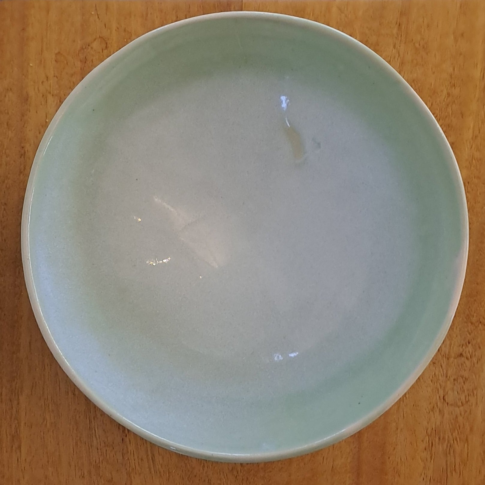 Green ceramic bowl on a wooden stand with a white background