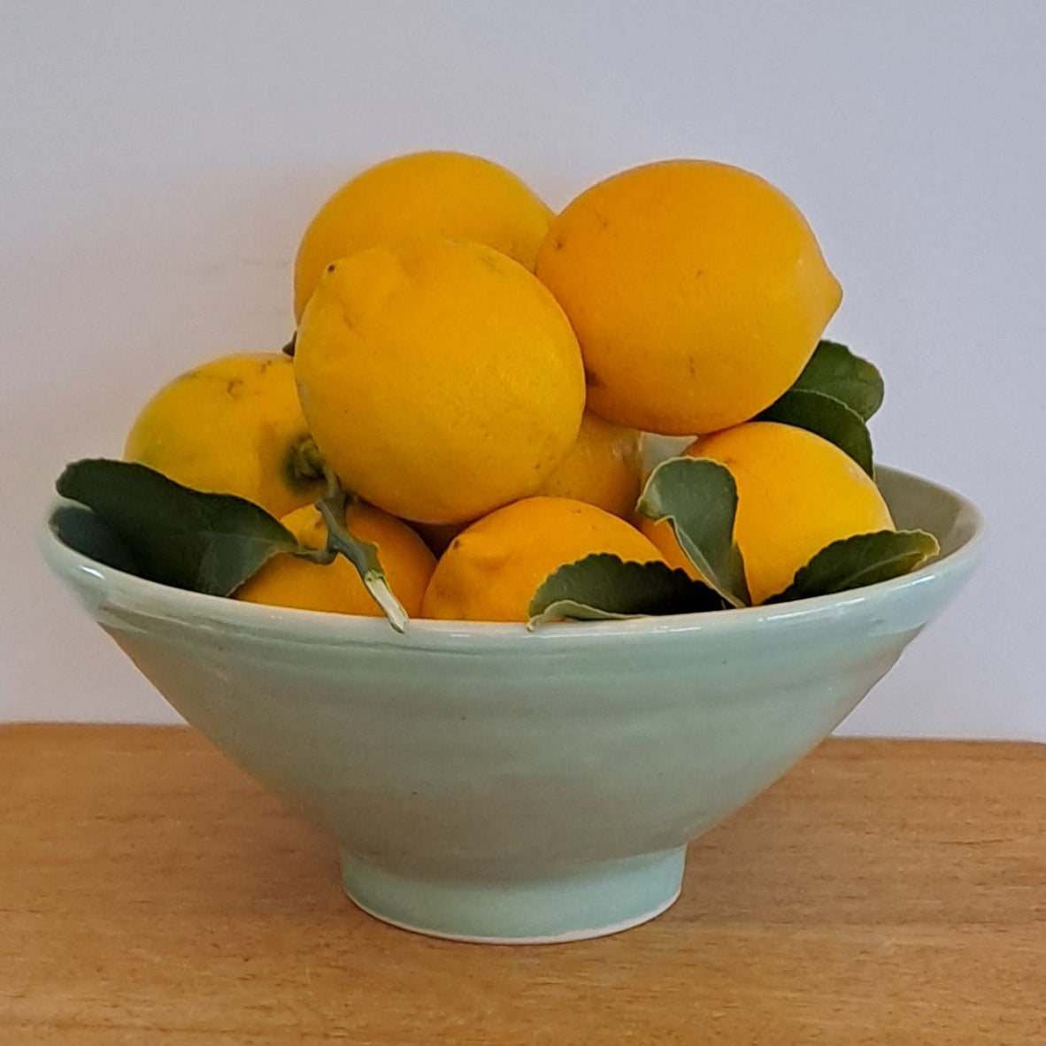 Yellow fruits in a green bowl on a wooden surface with a white background