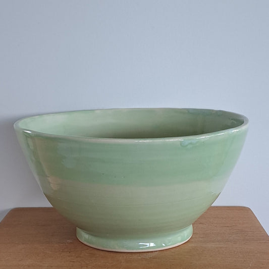 Green ceramic bowl on a wooden shelf against a white wall