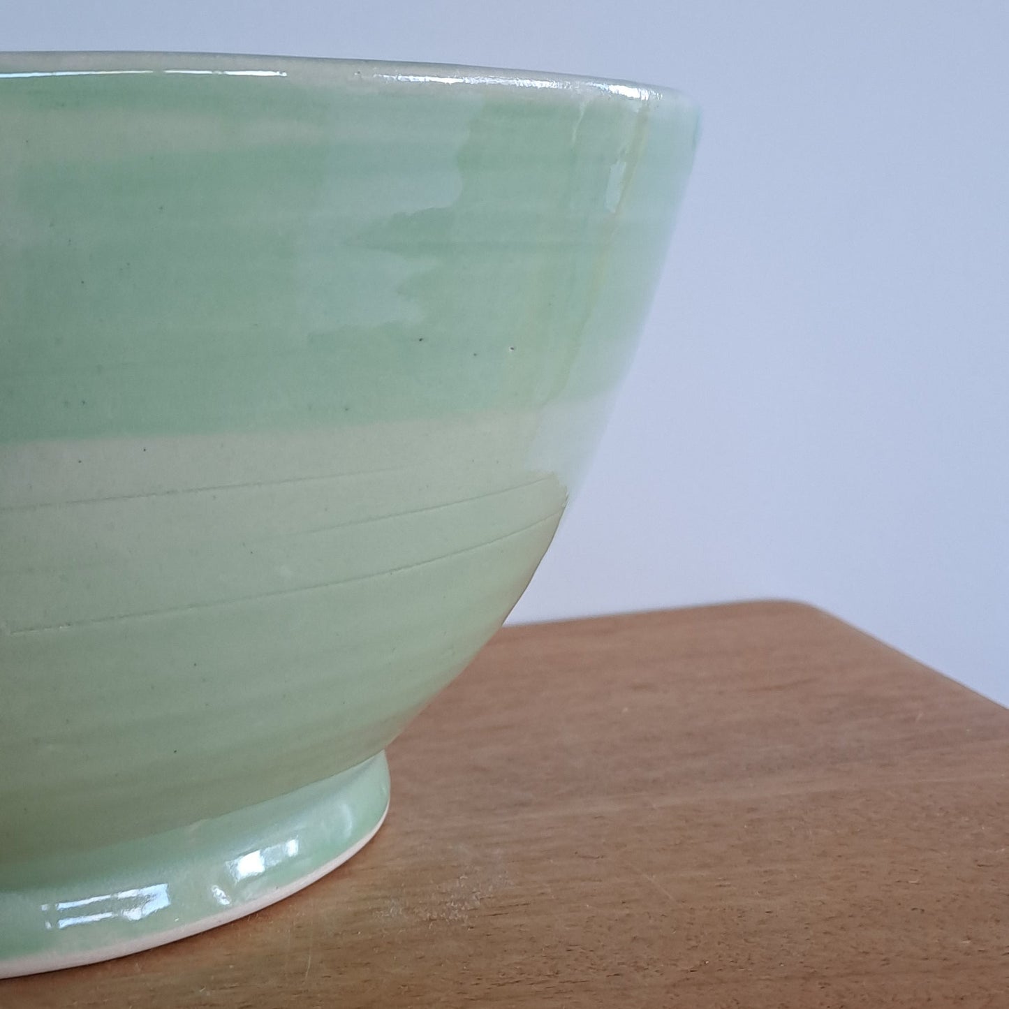Green ceramic bowl on a wooden surface with a light blue background