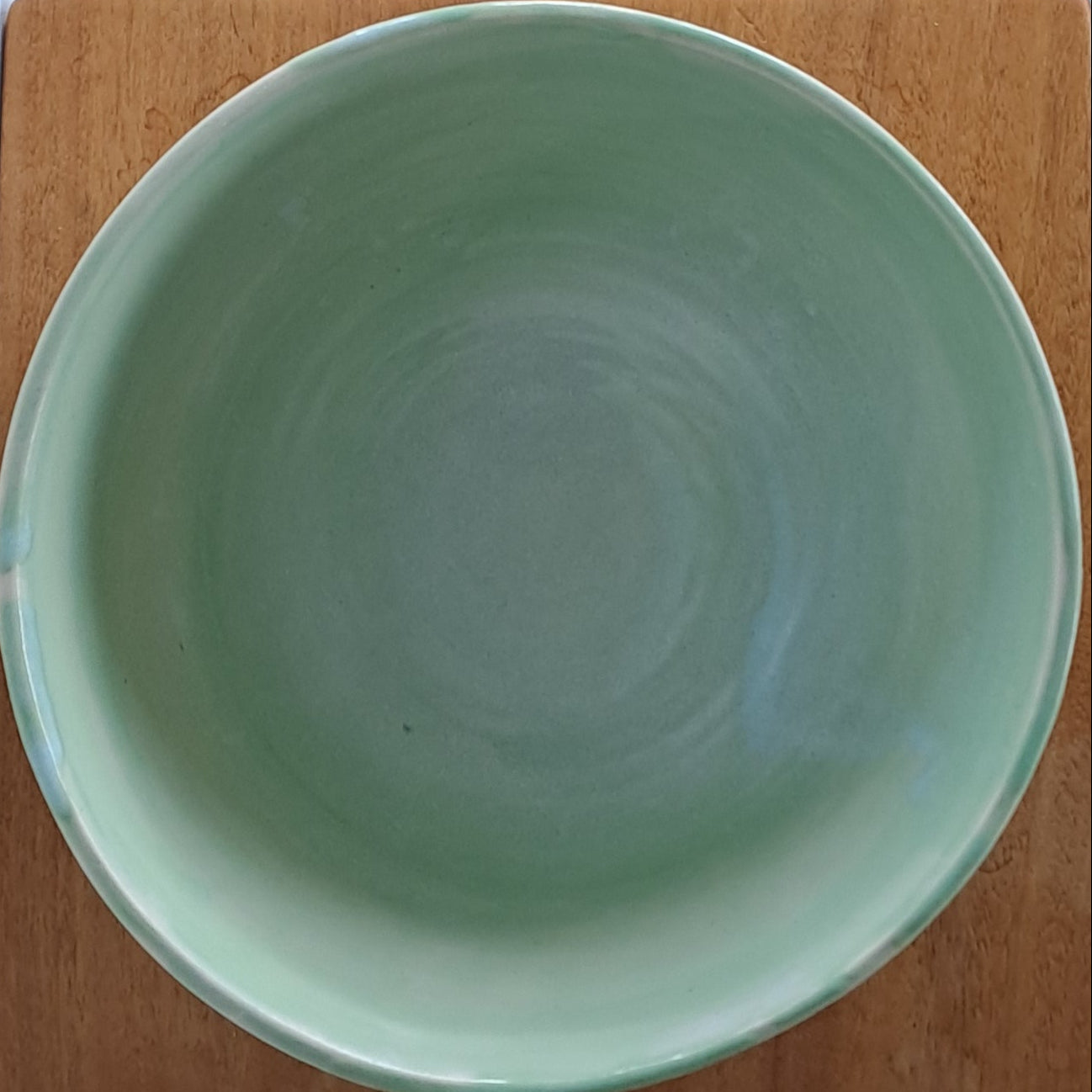 Green ceramic bowl on a wooden stand with a wooden surface and fabric in the background