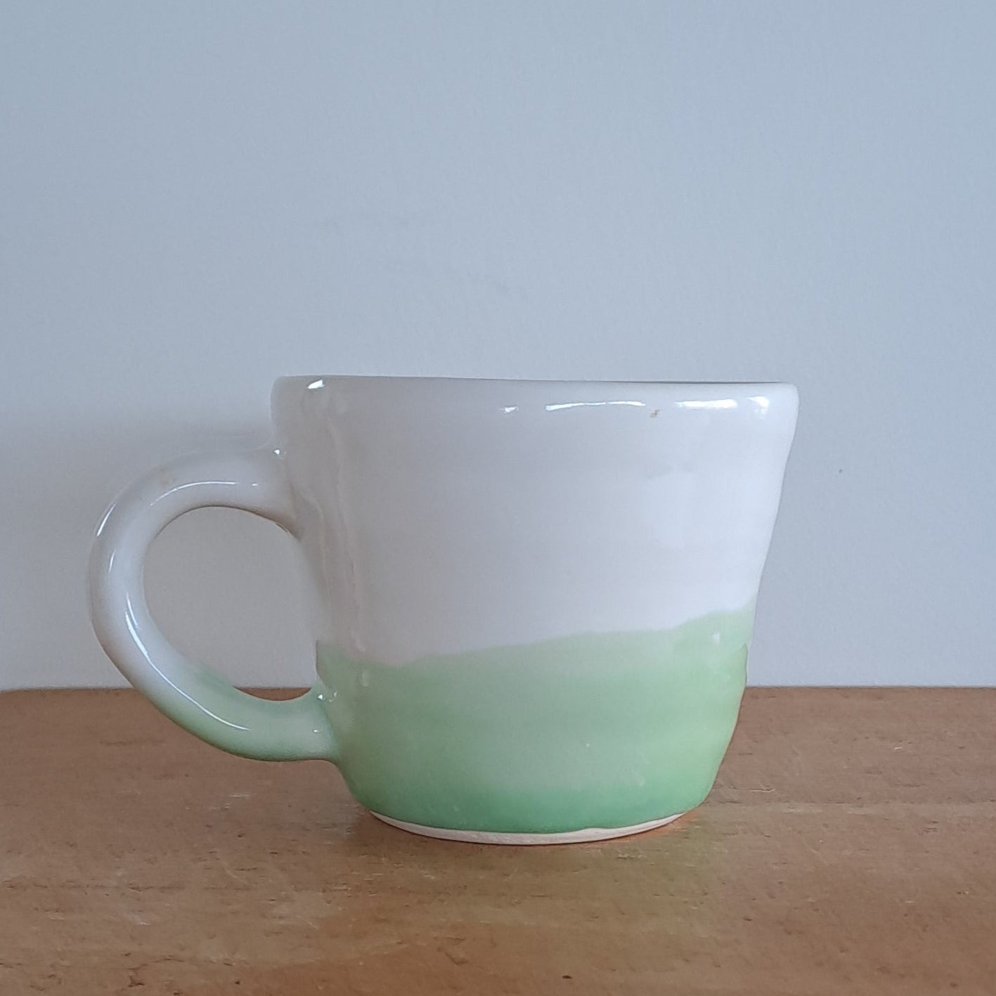 White and green cup on a wooden chair against a white wall