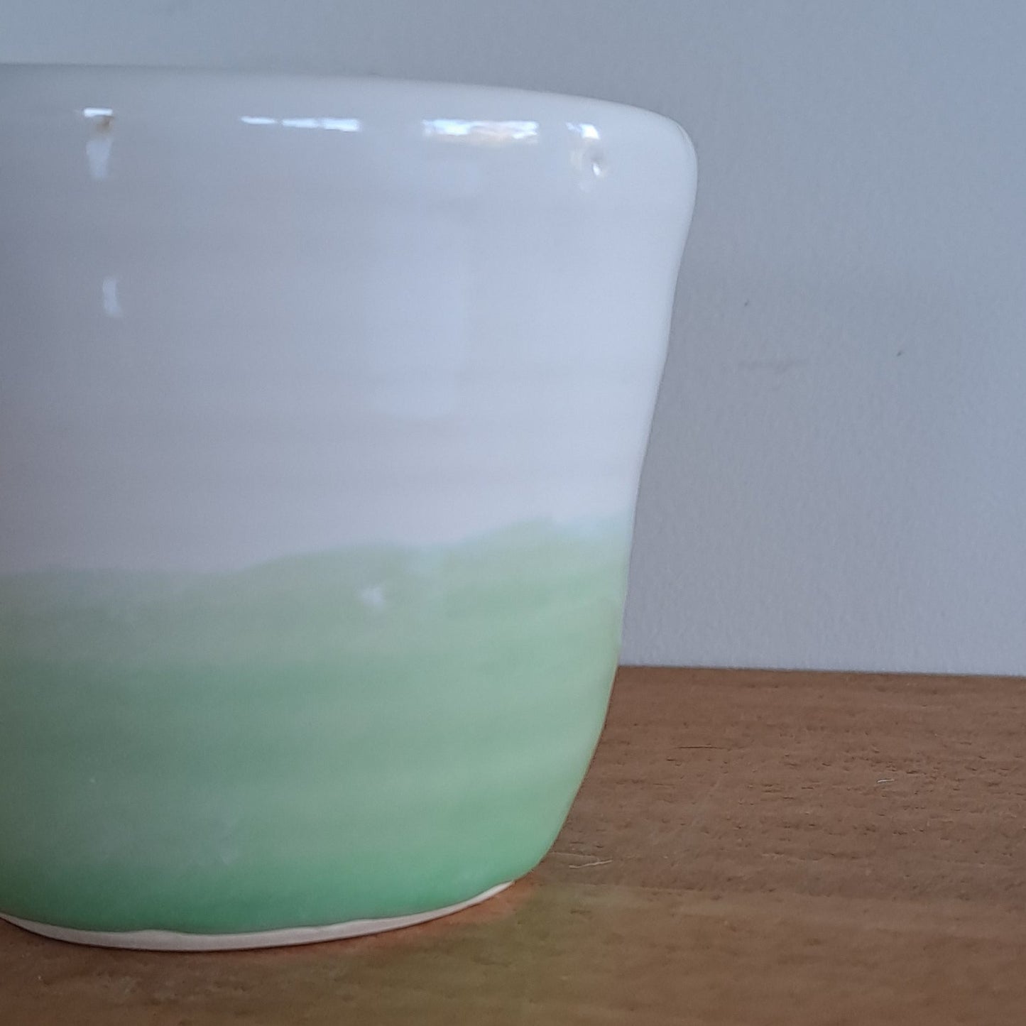 Green and white ceramic cup on a wooden surface with a white background