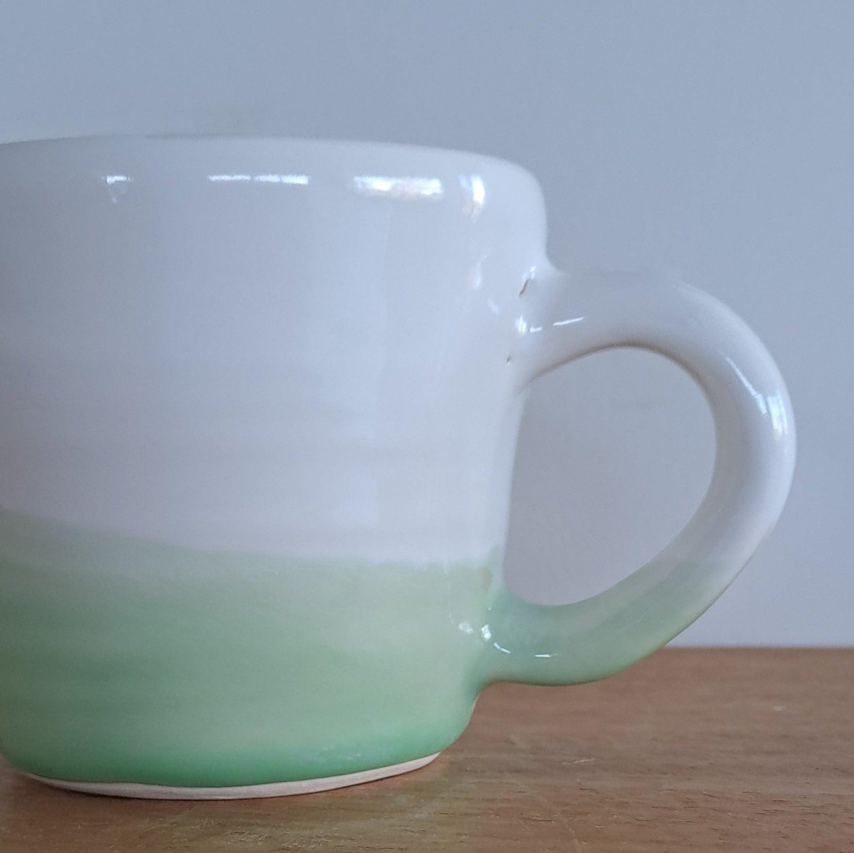 White mug with a green handle on a wooden surface