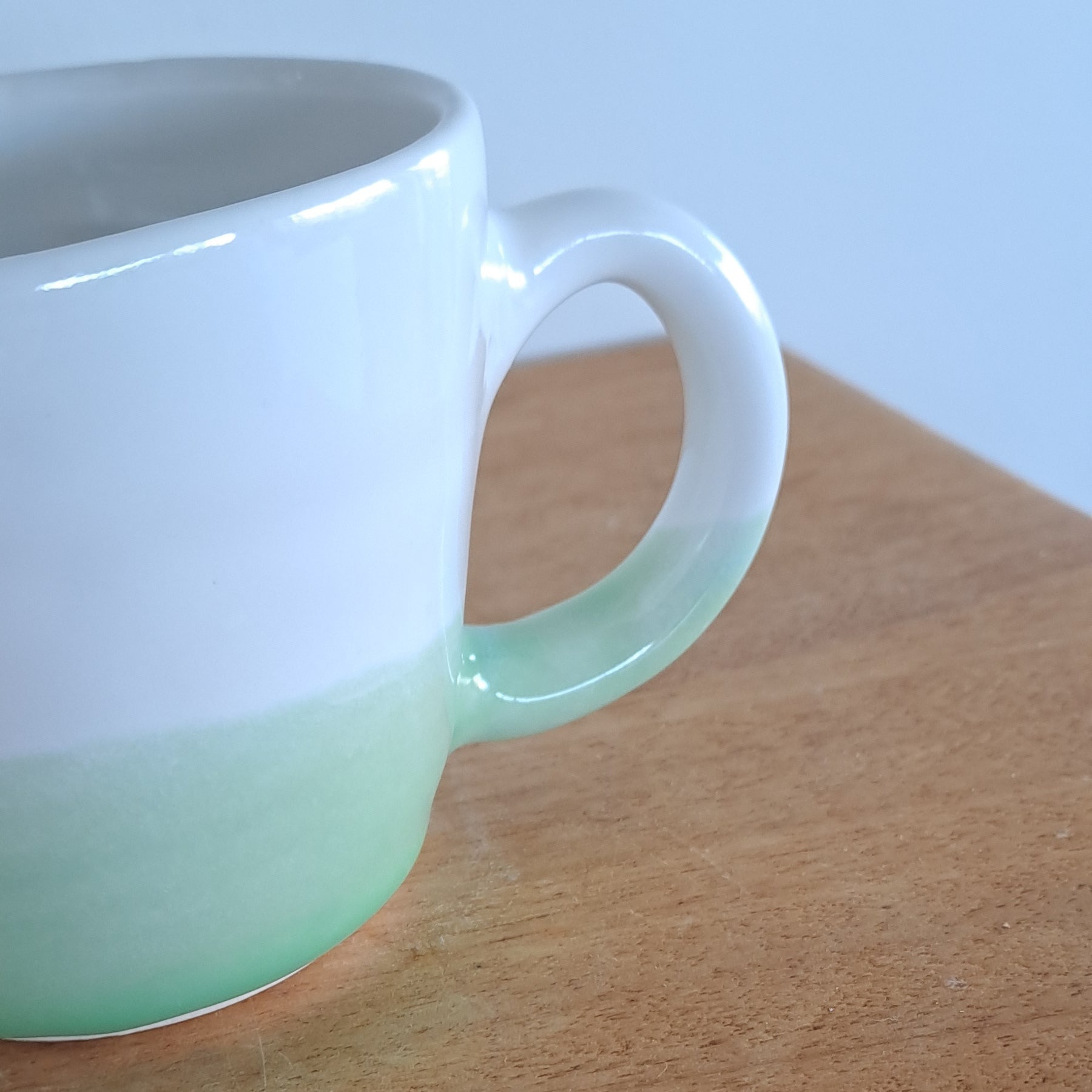 White and green ceramic cup on a wooden surface with a light blue background
