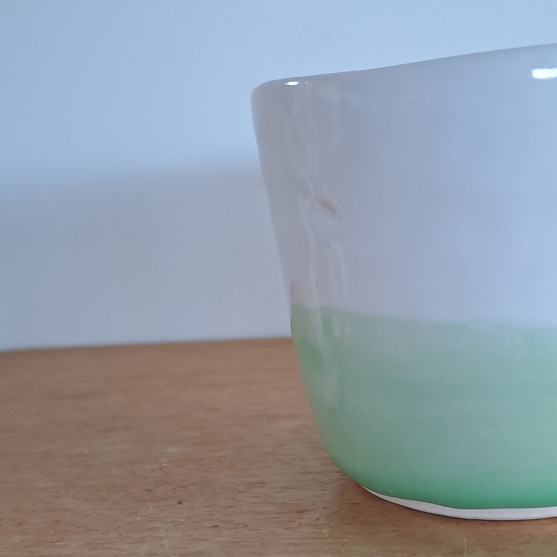 Green cup on a wooden surface with a white wall in the background