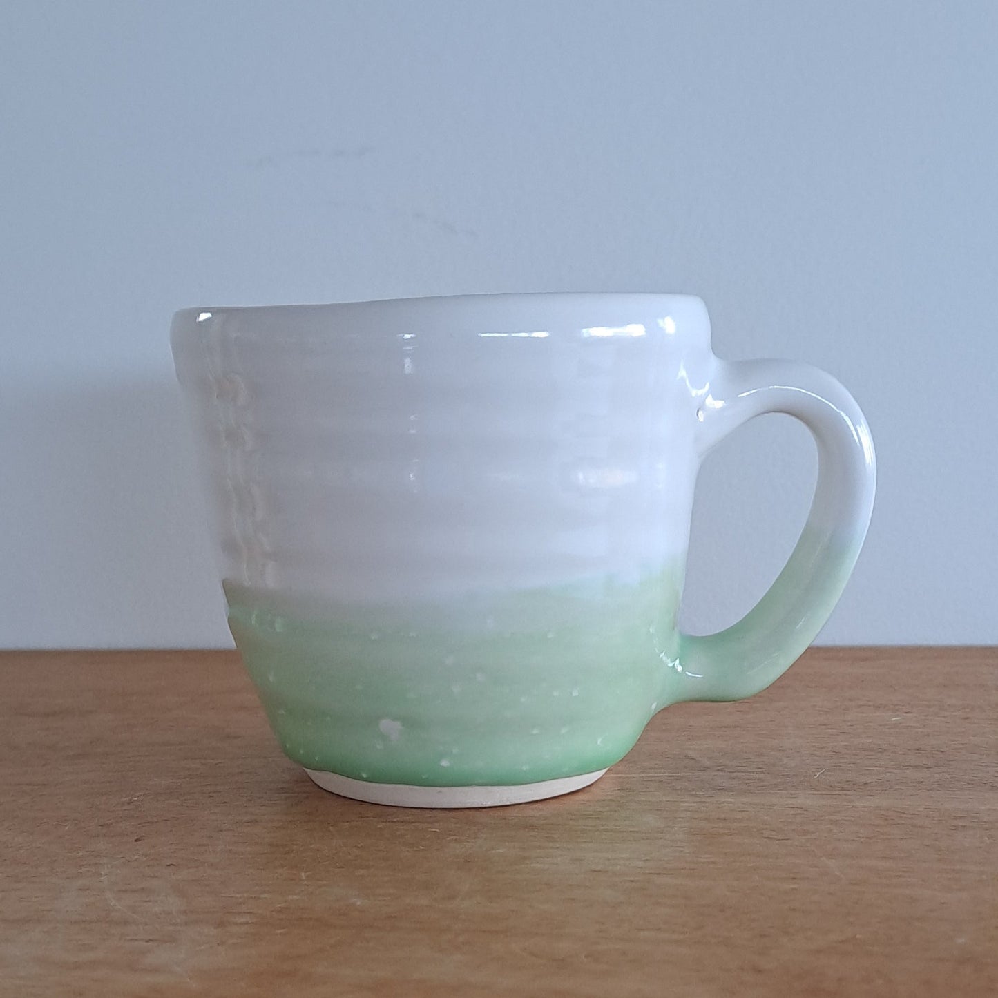 Green ceramic mug leaning against a wooden surface with a white wall background