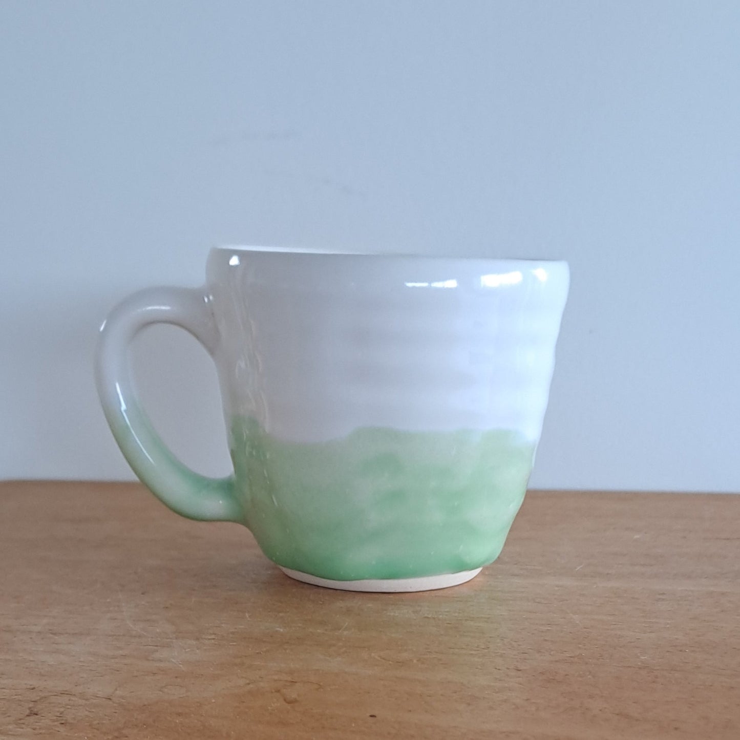 Green mug attached to a wooden surface with a white wall background