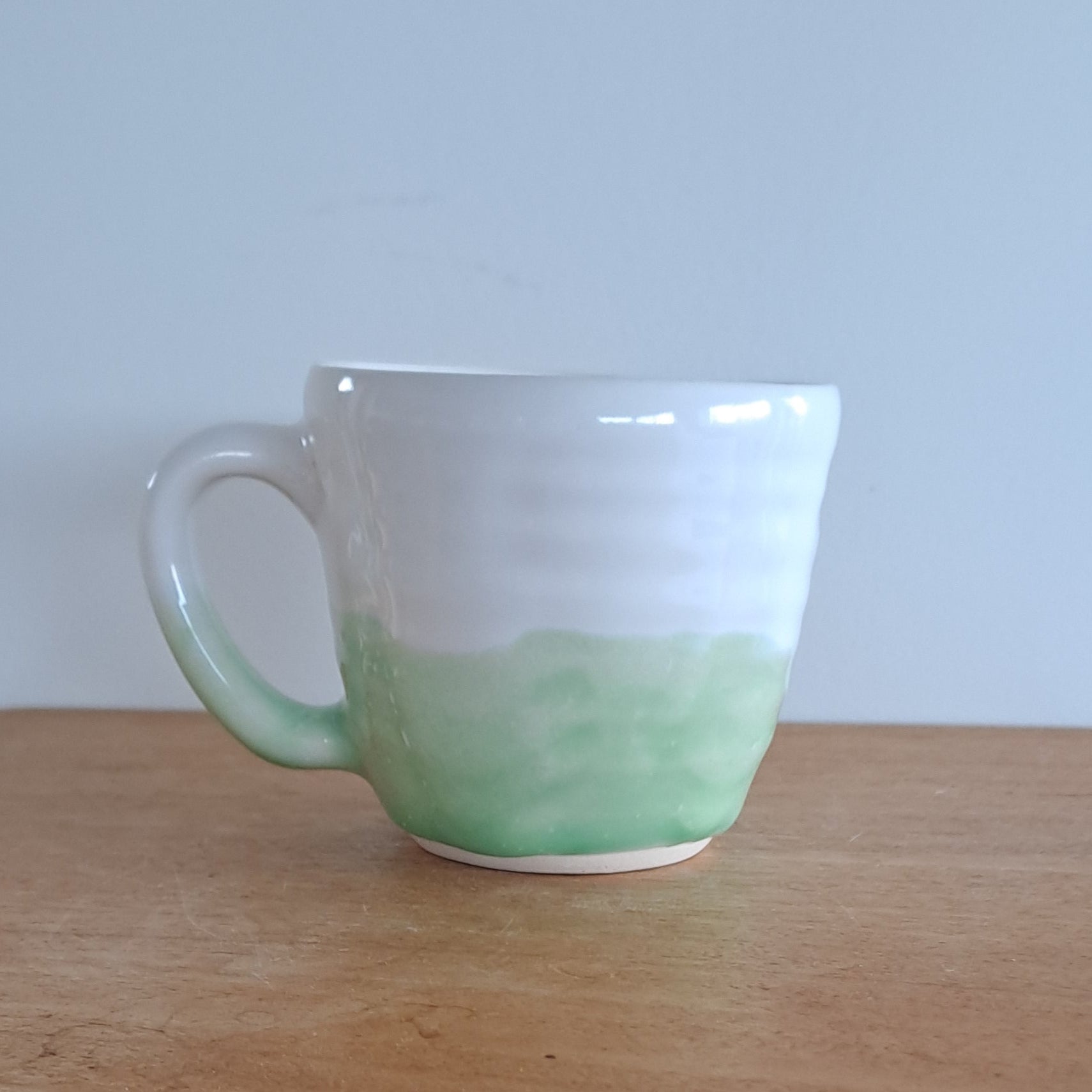 Green mug attached to a wooden surface with a white wall background