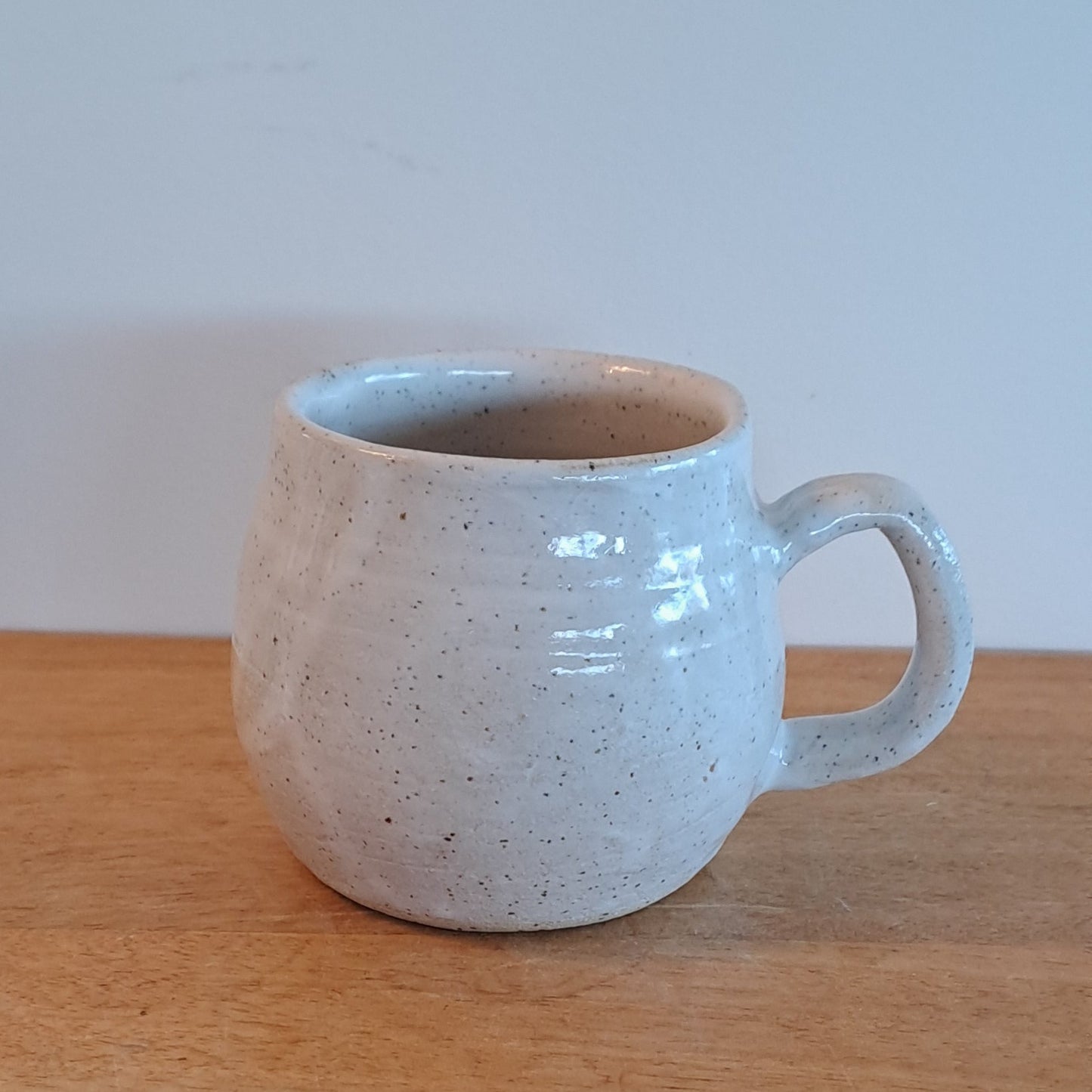 White ceramic cup on a wooden surface with a light blue wall background