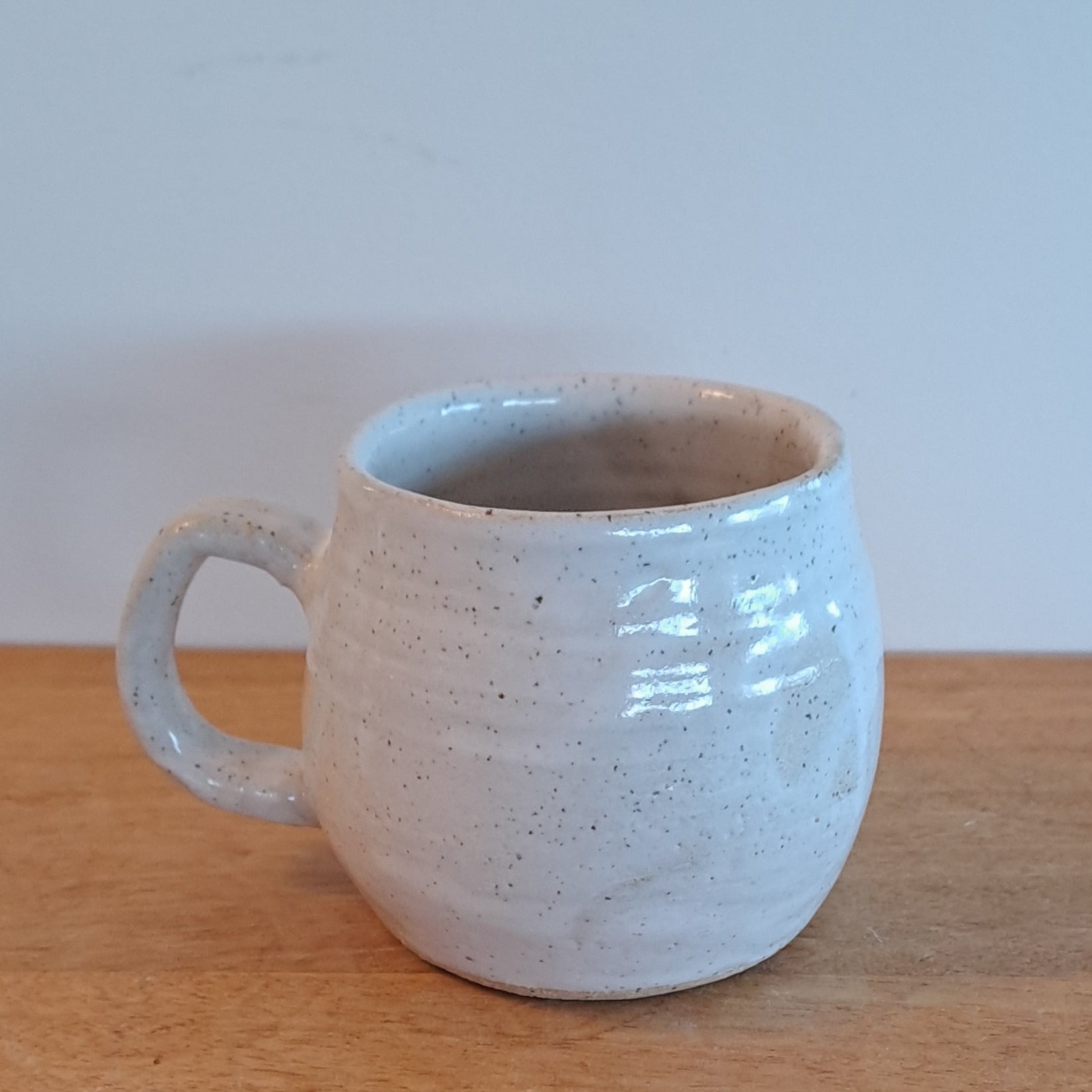 White ceramic cup leaning against a wooden surface with a light blue wall in the background
