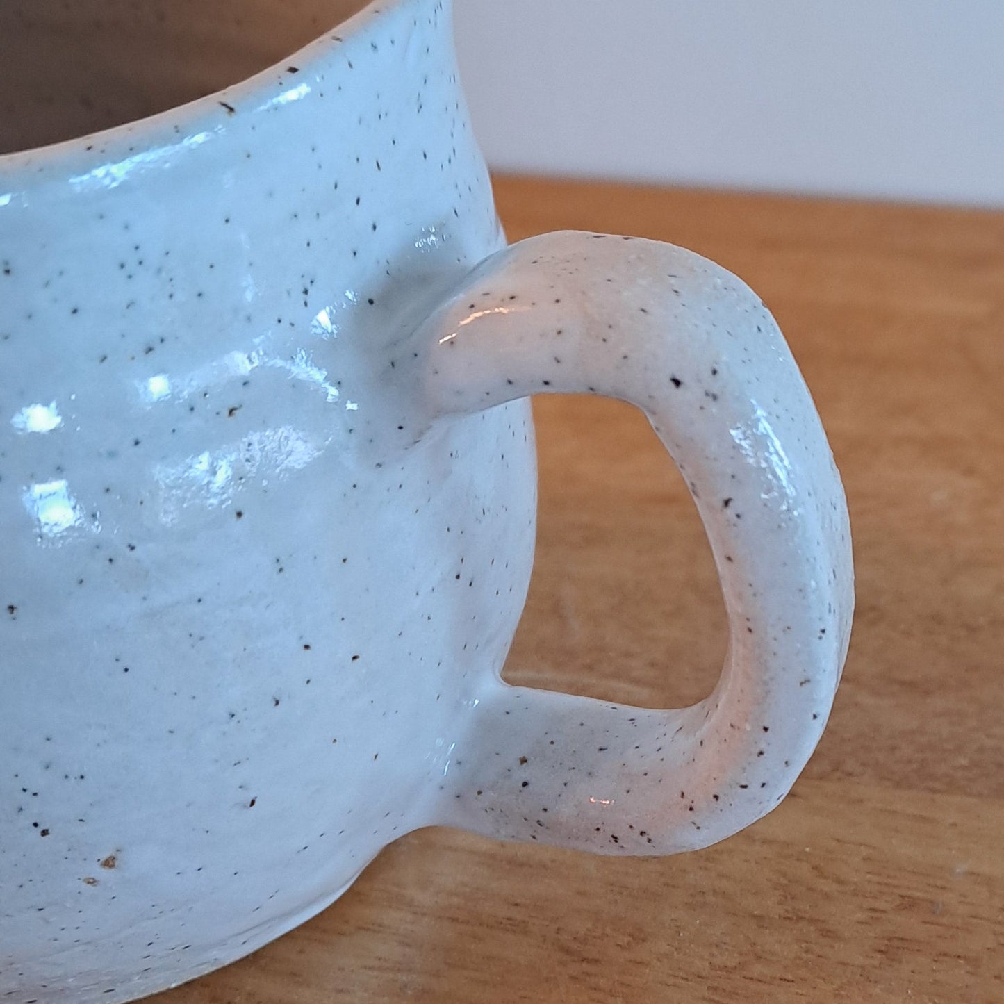 White ceramic mug with speckled texture and handle on a wooden surface