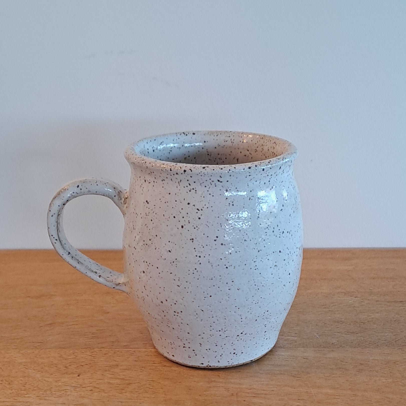 White ceramic cup with speckled texture on a wooden surface