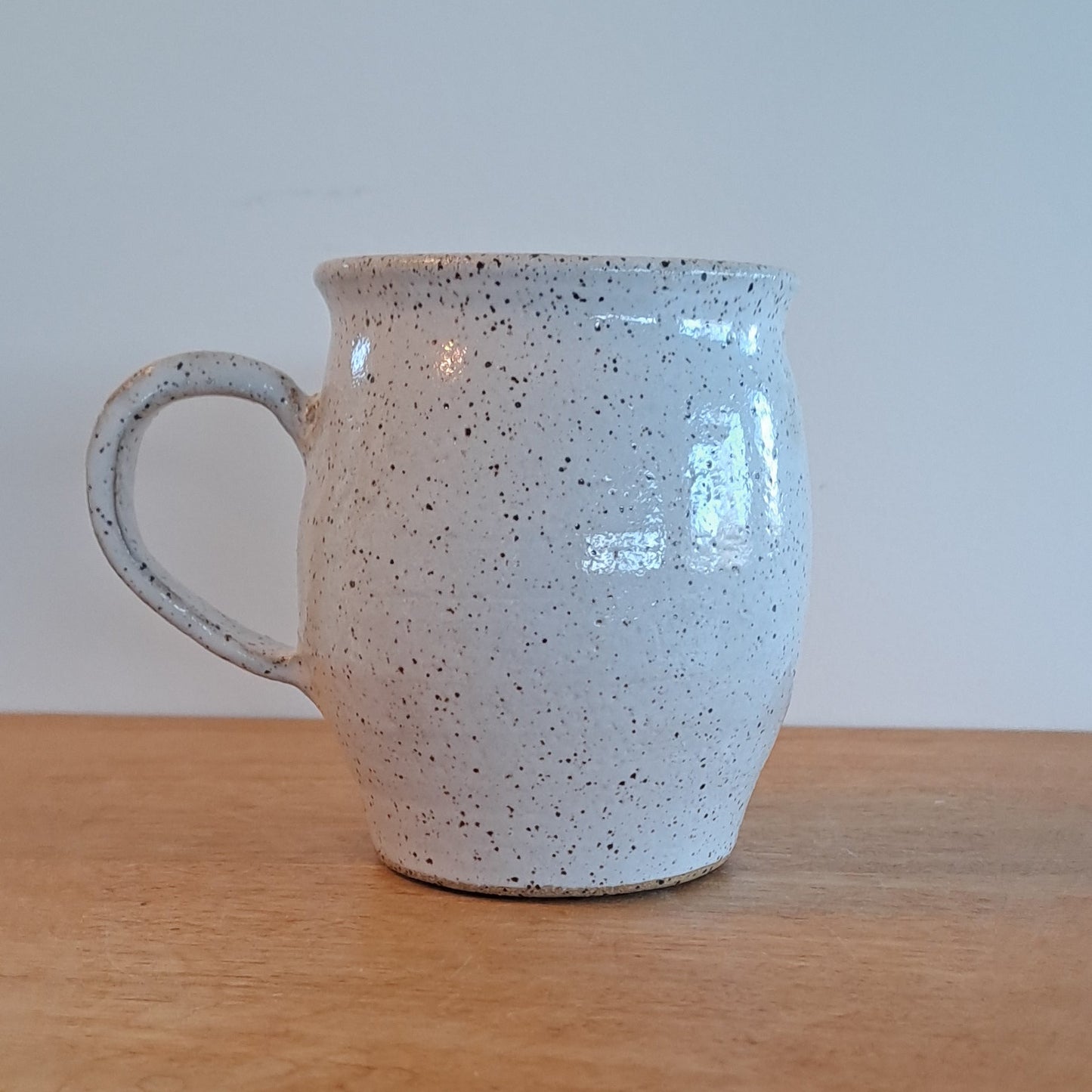 Speckled ceramic mug leaning against a wooden surface with a light gray wall background