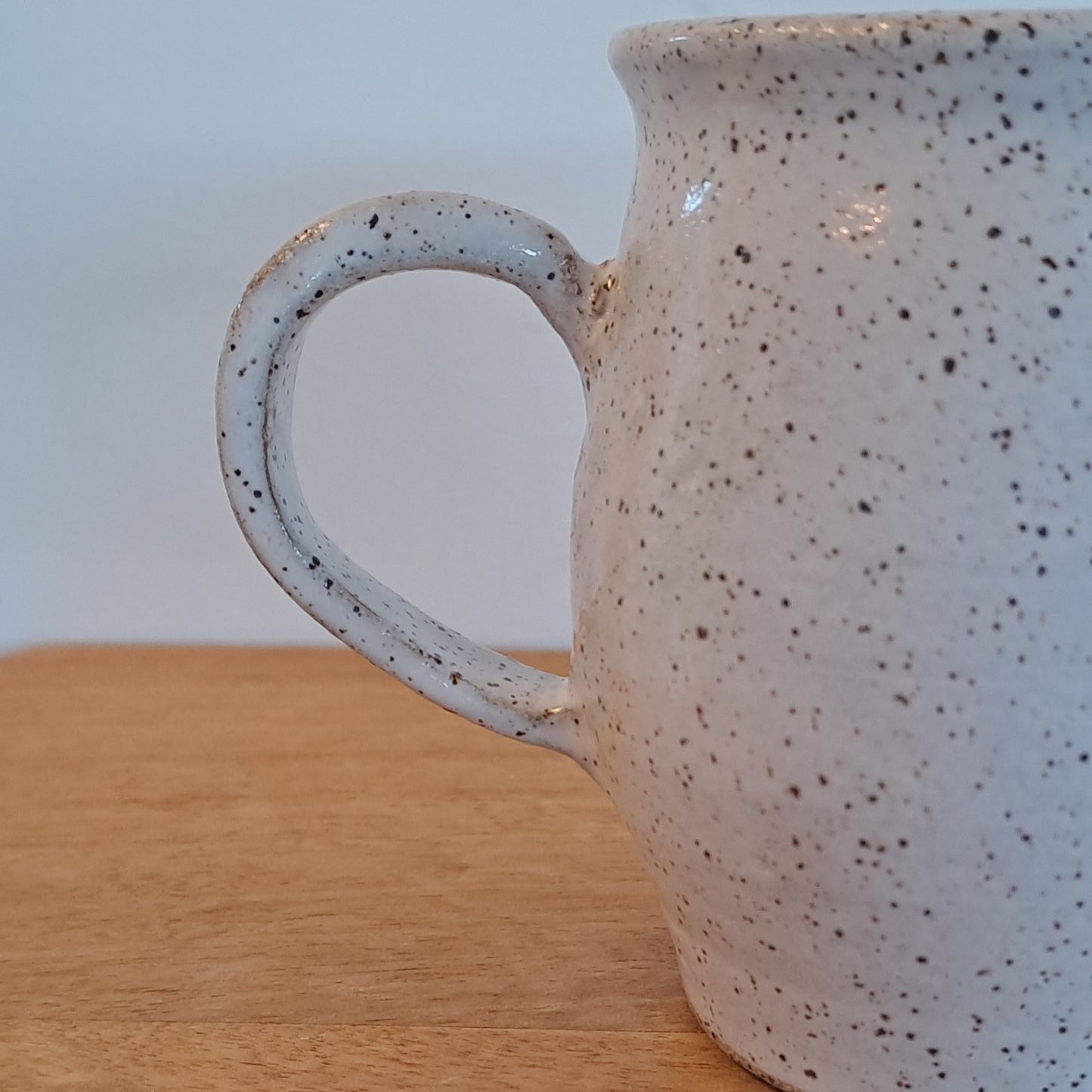 Speckled ceramic mug on a wooden surface with a white background