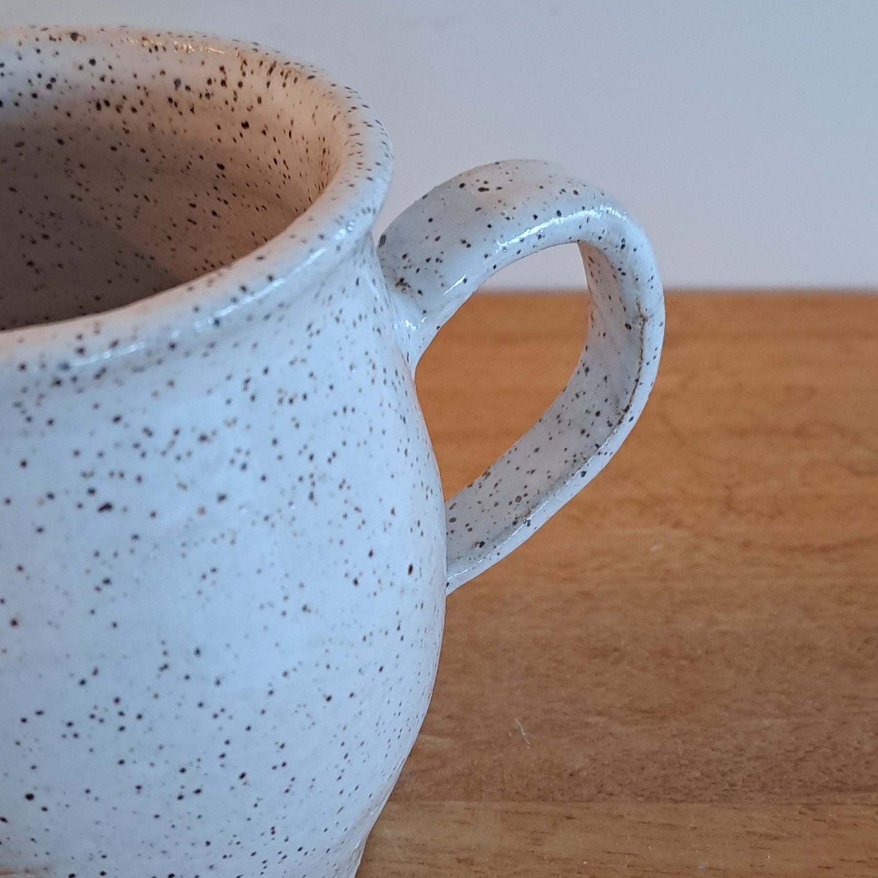 Speckled ceramic mug on a wooden surface with a white background