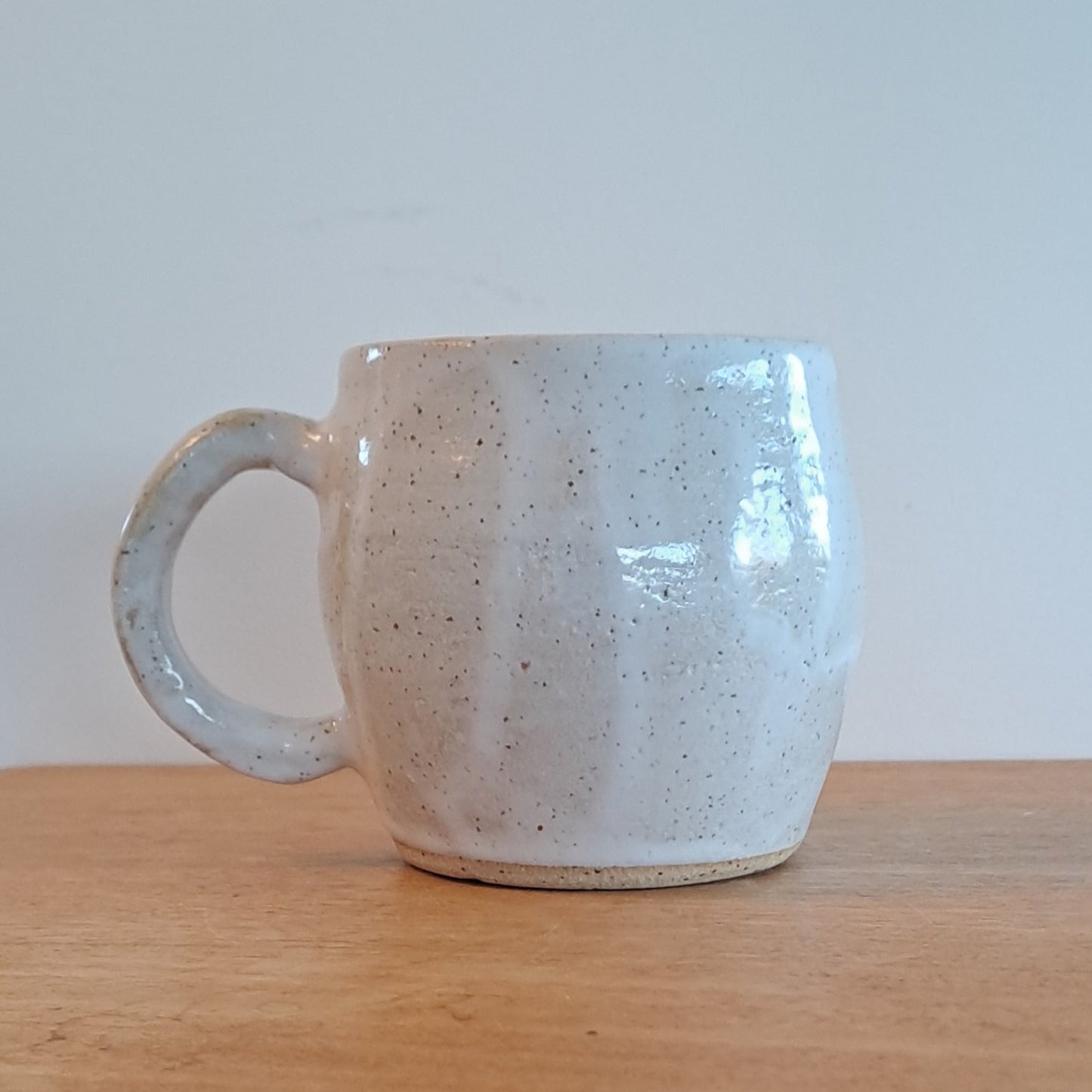 Ceramic mug with a textured surface on a wooden shelf against a white wall.