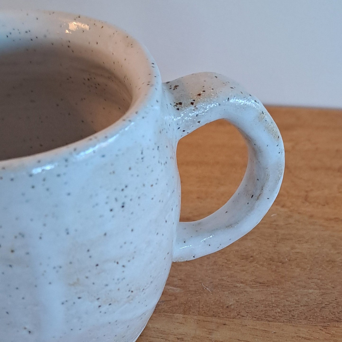 White ceramic mug with speckled texture on a wooden surface