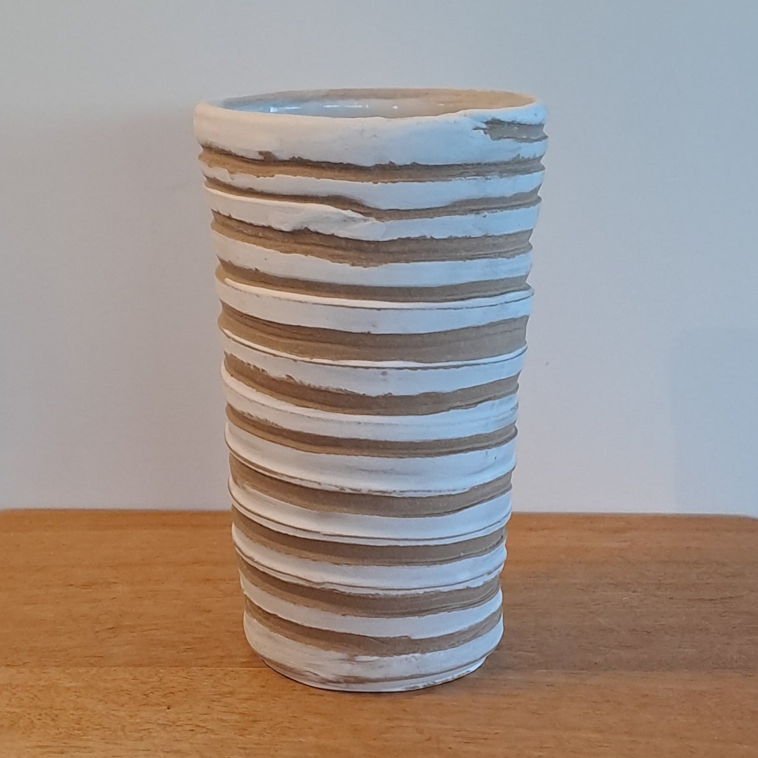 Wooden shelf with a cylindrical striped vase on a light background