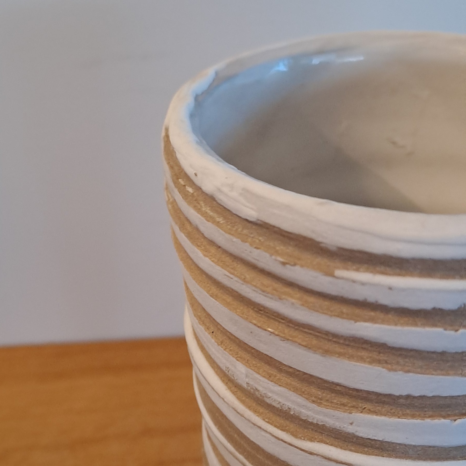 Close-up of a coiled white vase on a wooden surface with a white background