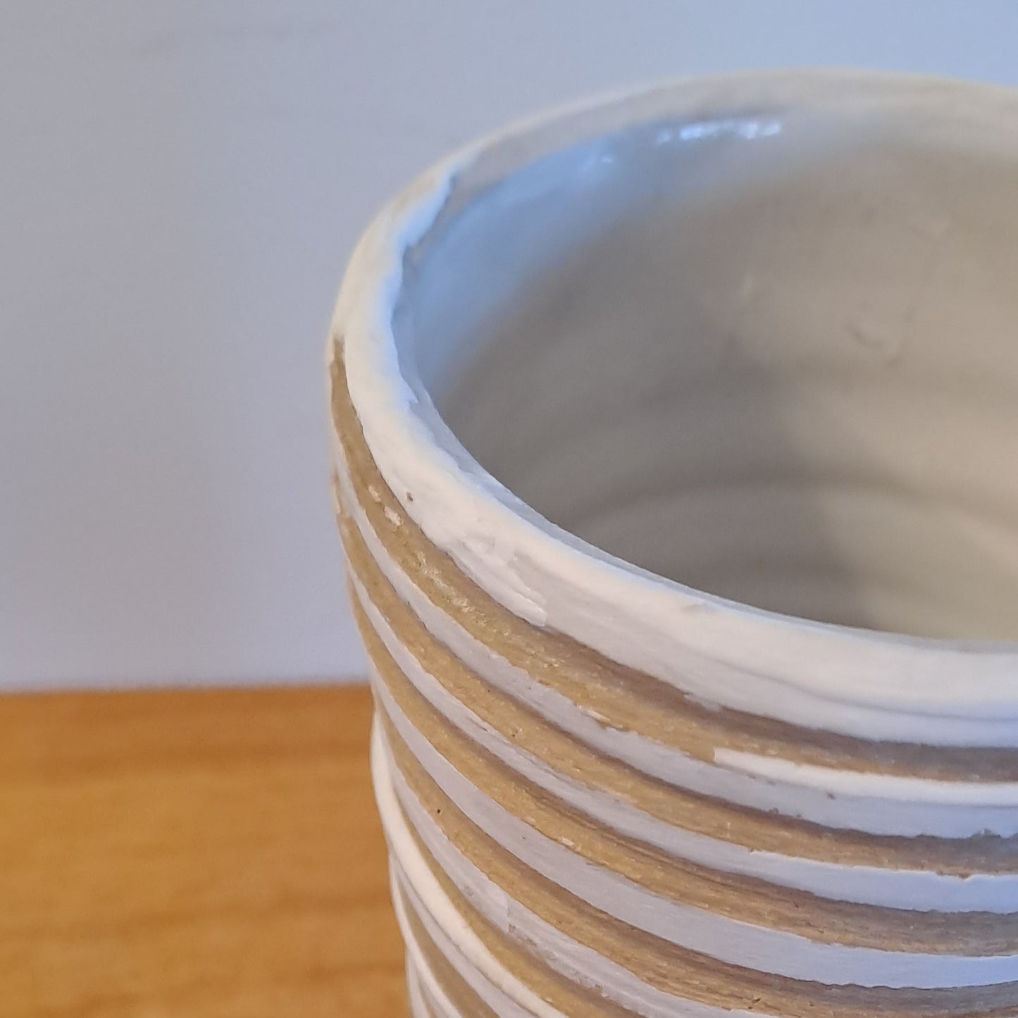 Close-up of a white cylindrical vase with concentric rings on a wooden surface.