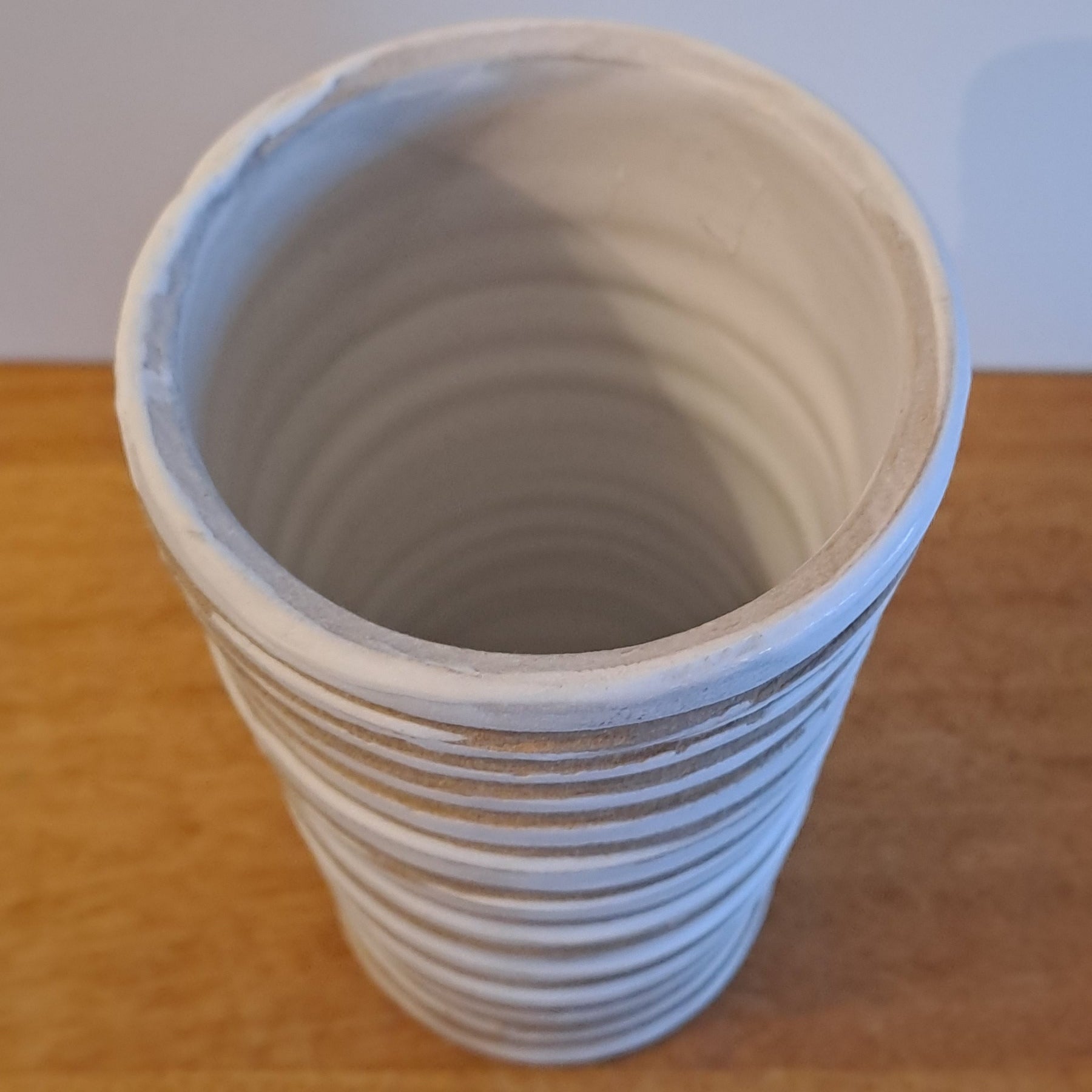 Wooden shelf with a cylindrical striped vase on a light background